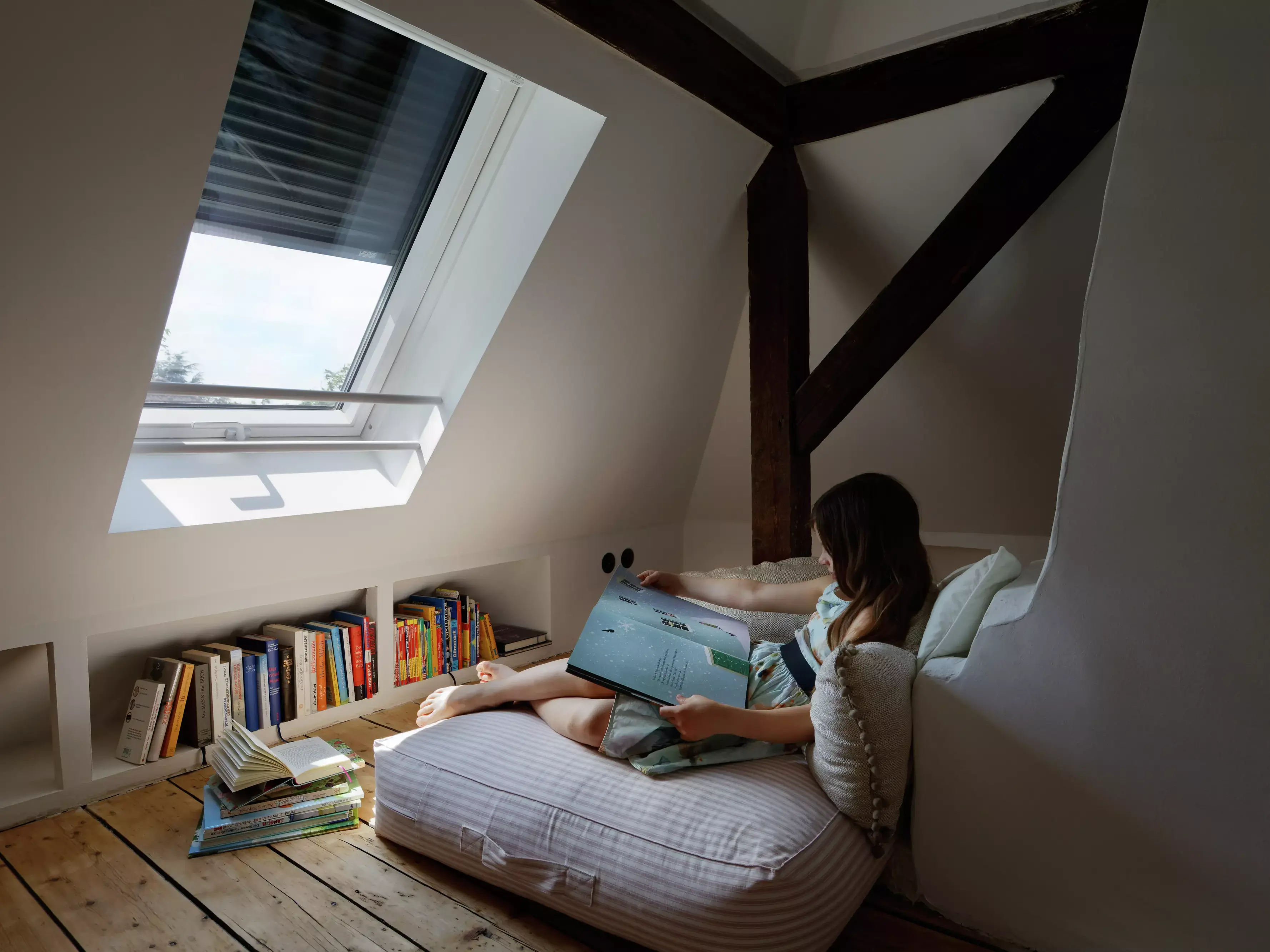Coin lecture cosy dans le comble avec fenêtre de toit VELUX et étagères.