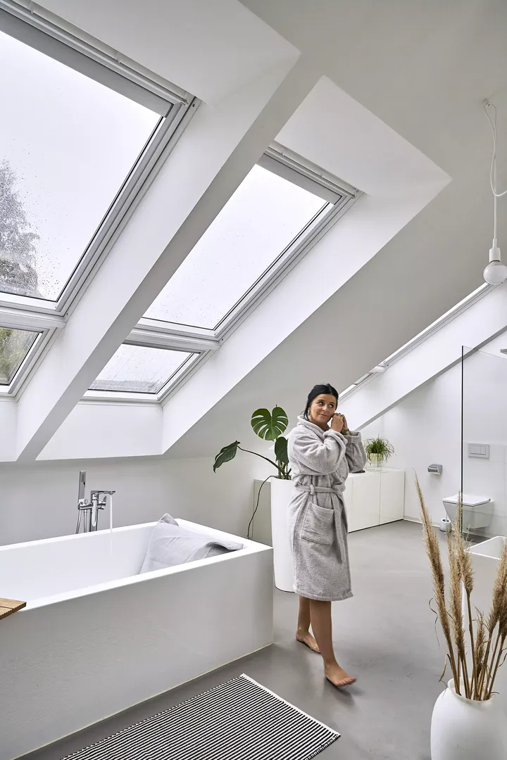 Modernes Badezimmer mit VELUX Dachflächenfenstern und weißer Badewanne, beleuchtet durch natürliches Licht.