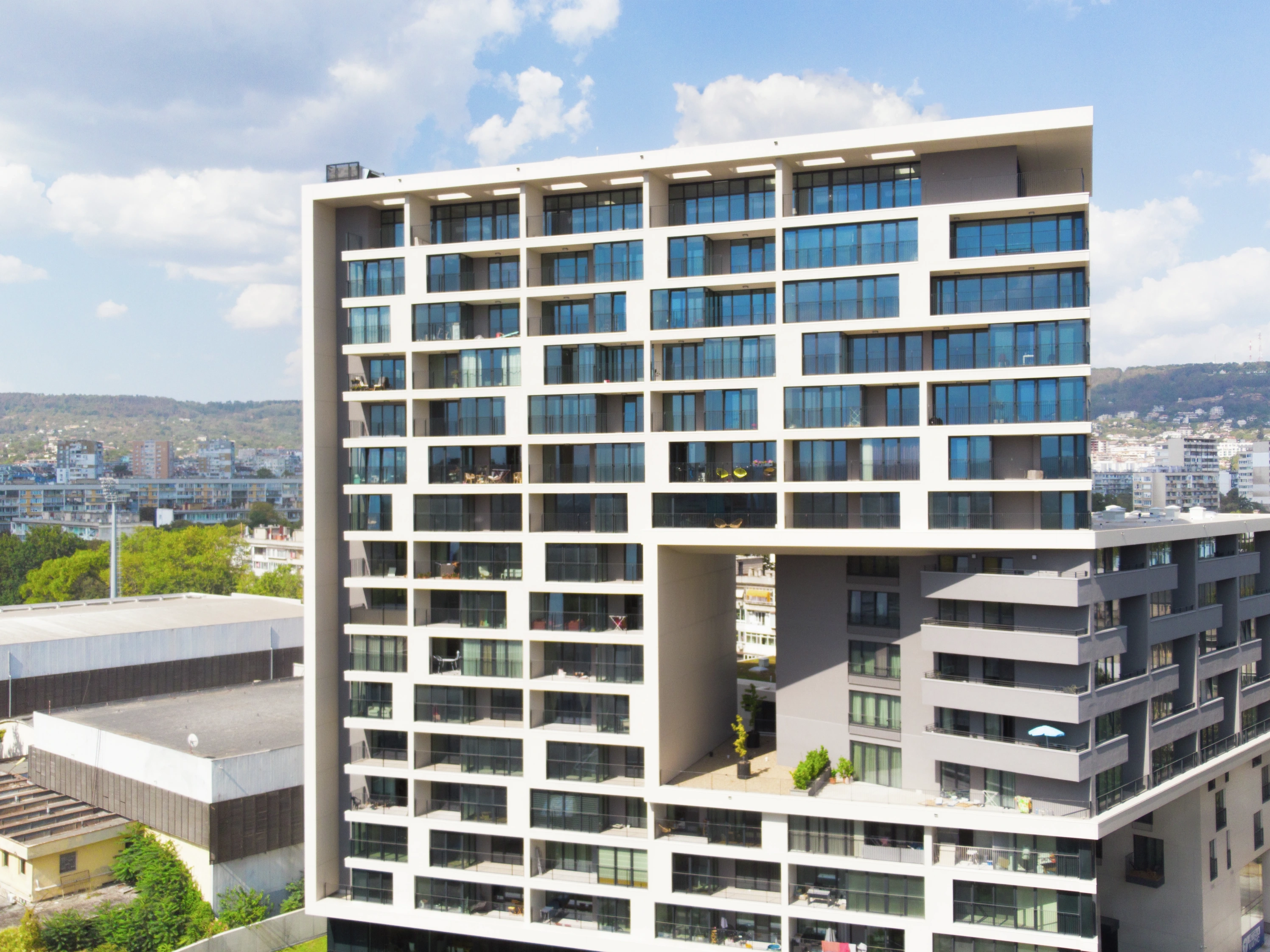 Contemporary high-rise apartment building with large glass balconies in a sunny cityscape.