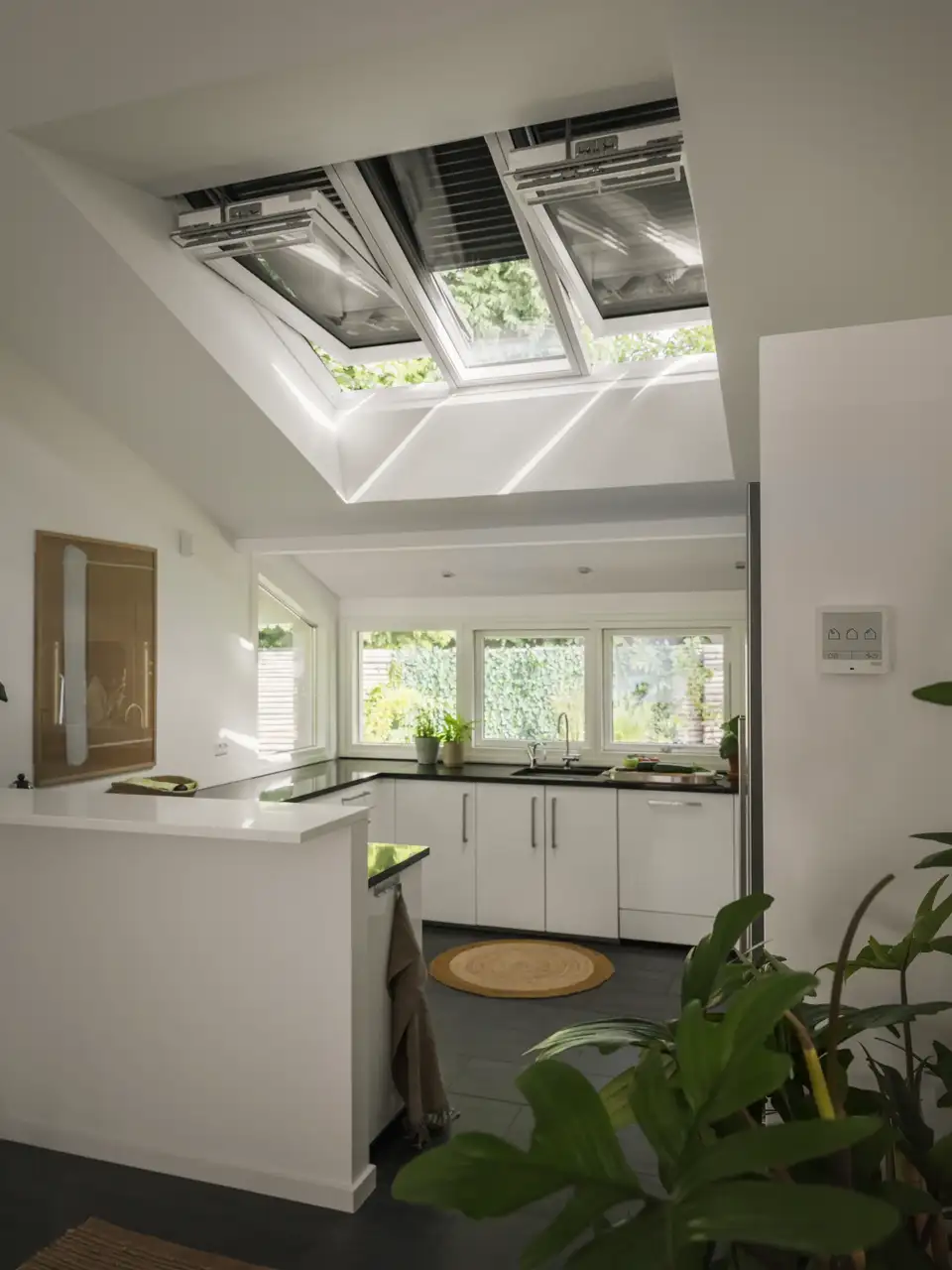 Una cocina iluminada por ventanas de fachada y ventanas de tejado VELUX equipadas con persianas de aluminio.