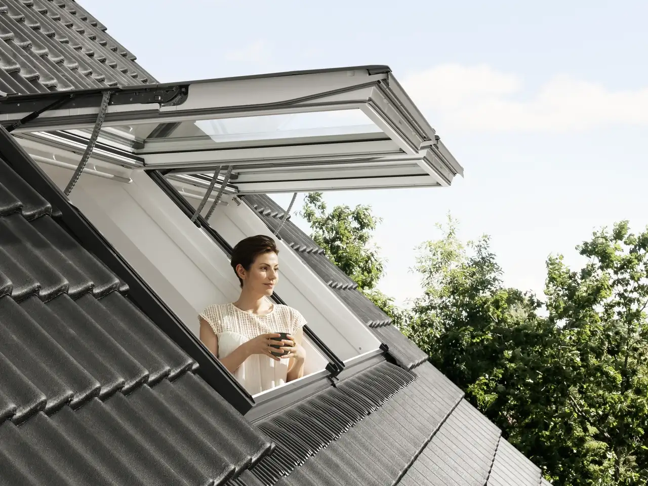 Eine Frau an ihrem VELUX-Dachfenster, das nach außen geöffnet ist | VELUX Magazin