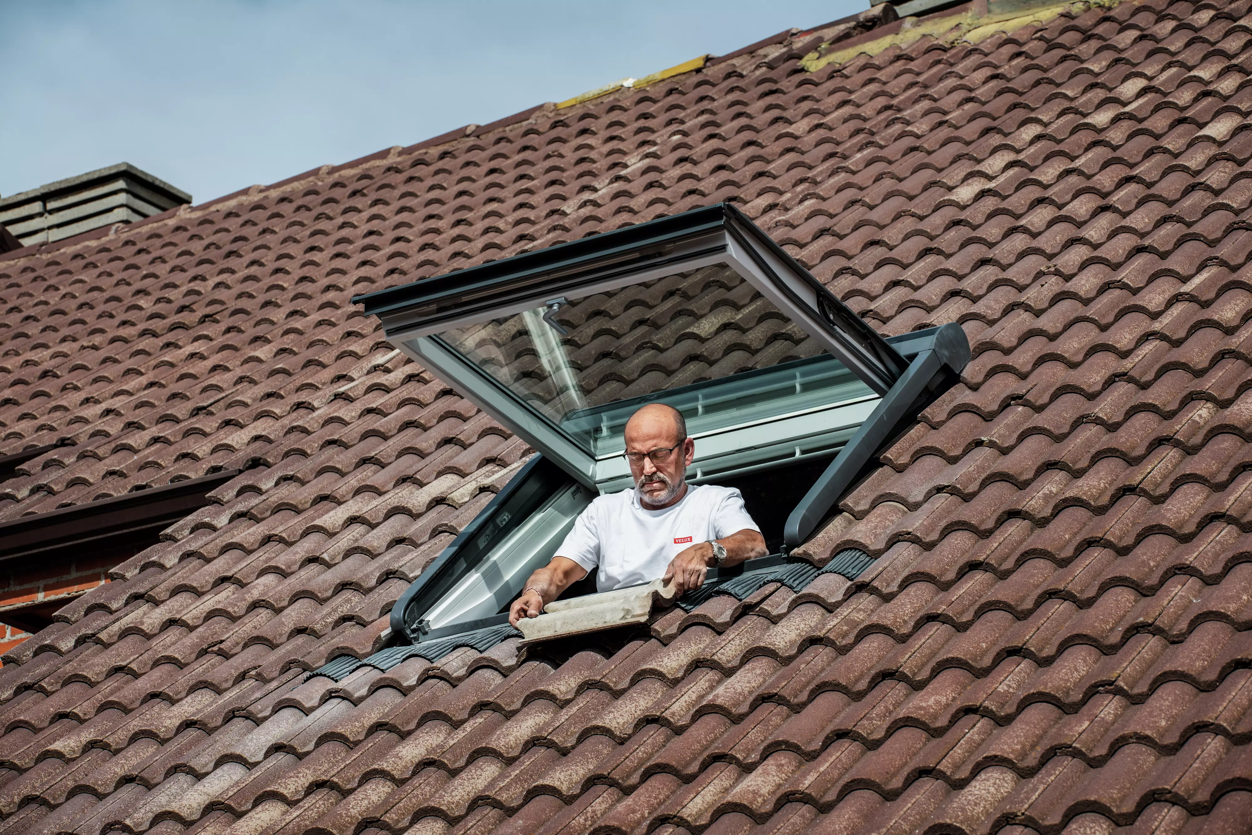 Technik pracujący przy montażu okna dachowego, sprawdzający prawidłowe ułożenie dachówek. | VELUX