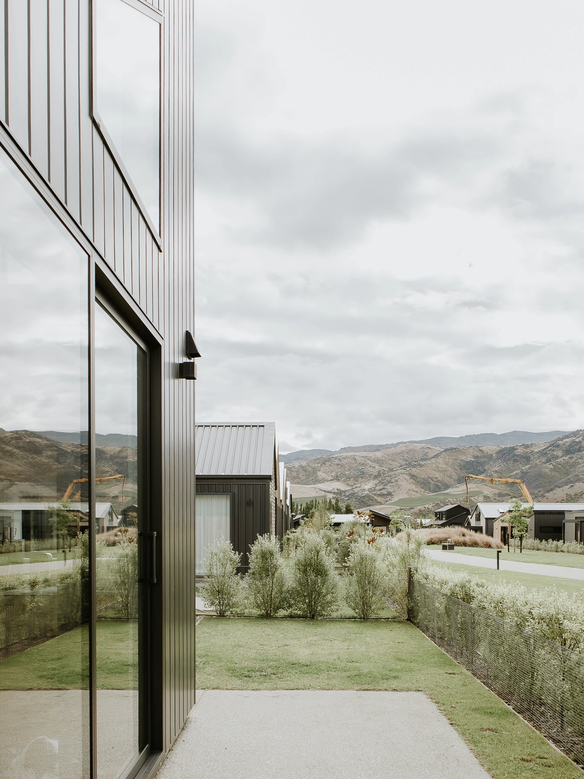 Modern metal-clad house with sliding glass door facing a green yard and distant hills.