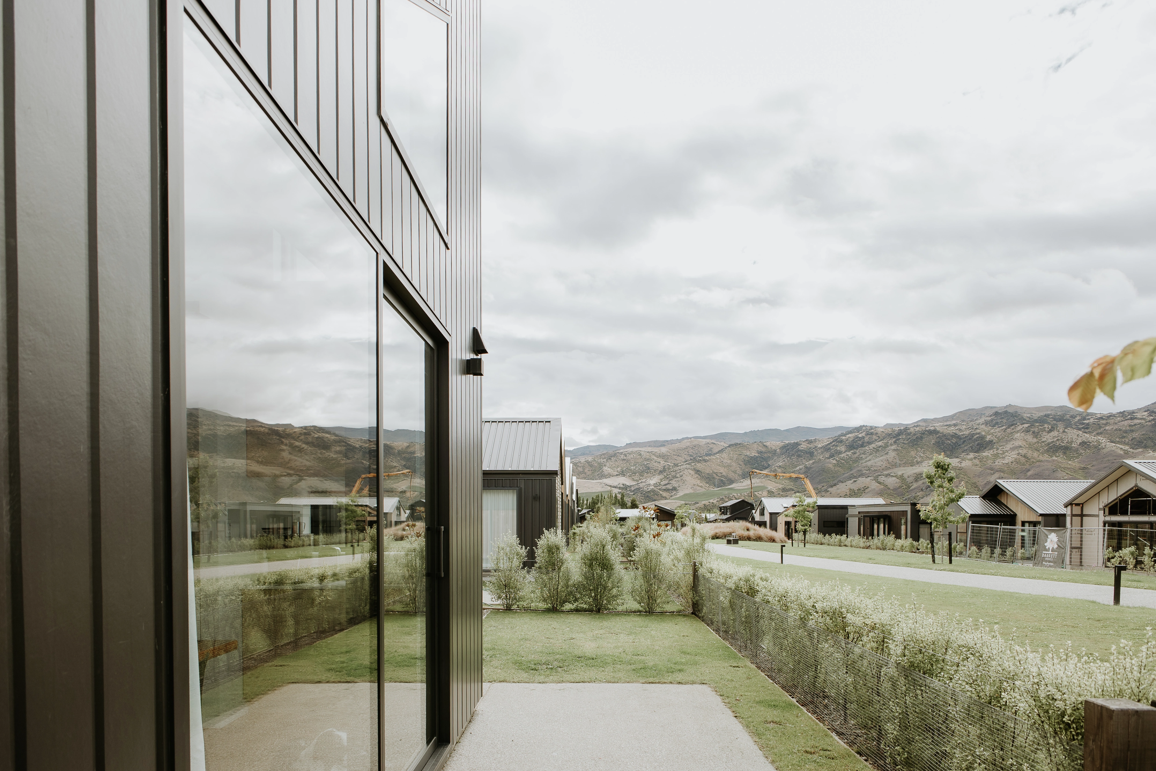 Modern metal-clad house with sliding glass door facing a green yard and distant hills.