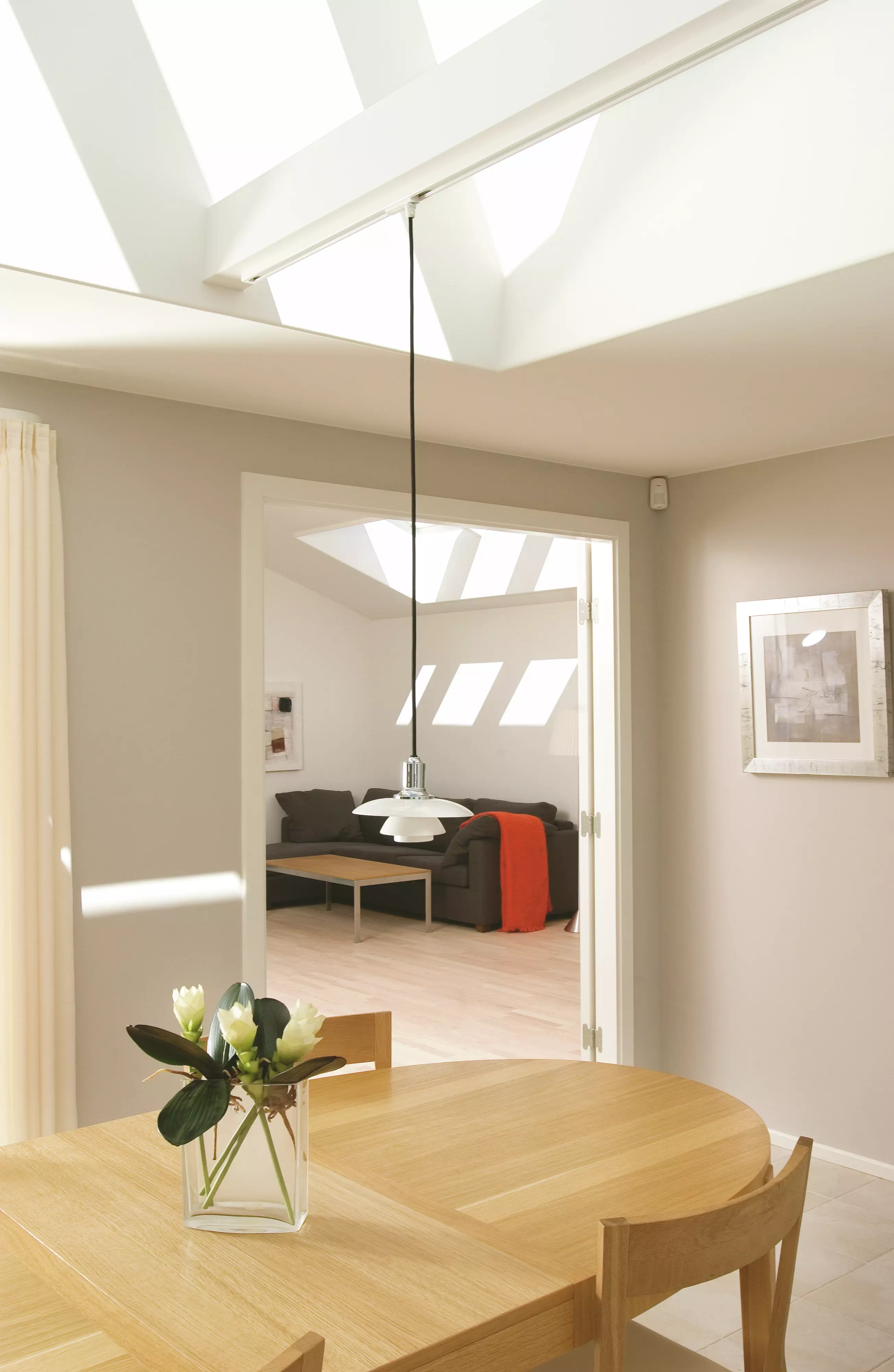 Salon moderne avec lumière naturelle provenant d'une fenêtre de toit VELUX, meubles en bois et accents rouges.
