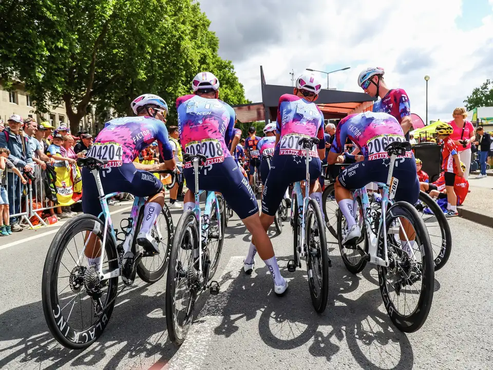 Kolesarji dirke Tour de France v pisanih dresih se pripravljajo na start, obkroženi z navijači, ki imajo na hrbtih VELUX številke.
