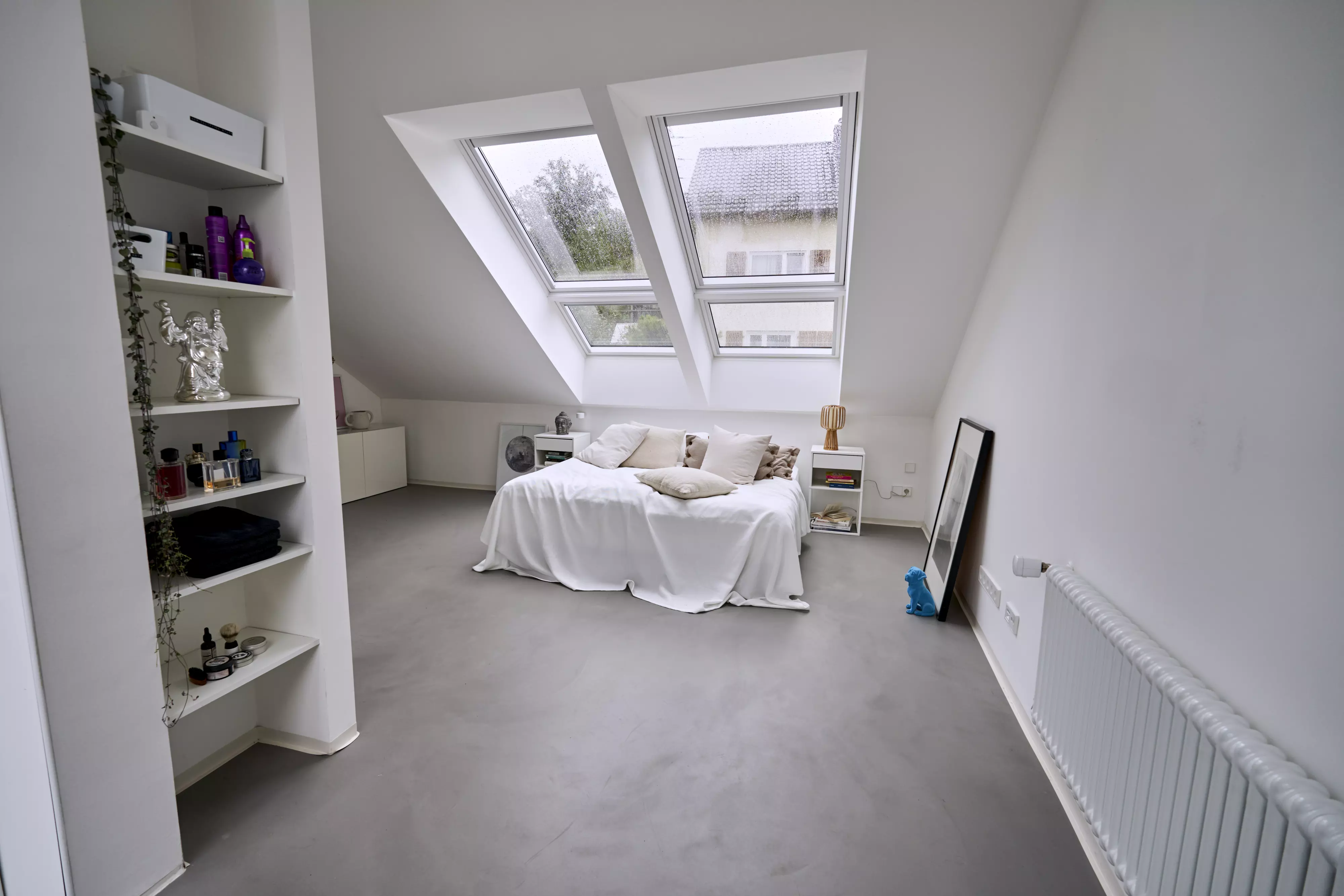 Schlafzimmer im Dachboden mit Bett, weißen Regalen, VELUX Dachflächenfenstern und einem anlehnenden Spiegel.