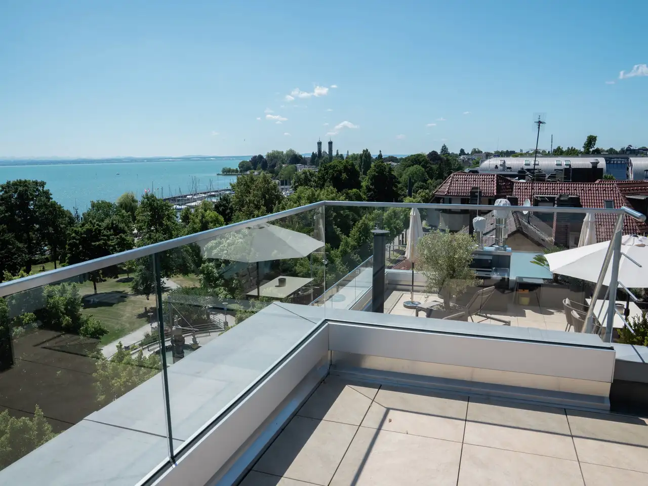 Rooftop terrace with glass railings overlooking a lake and greenery.