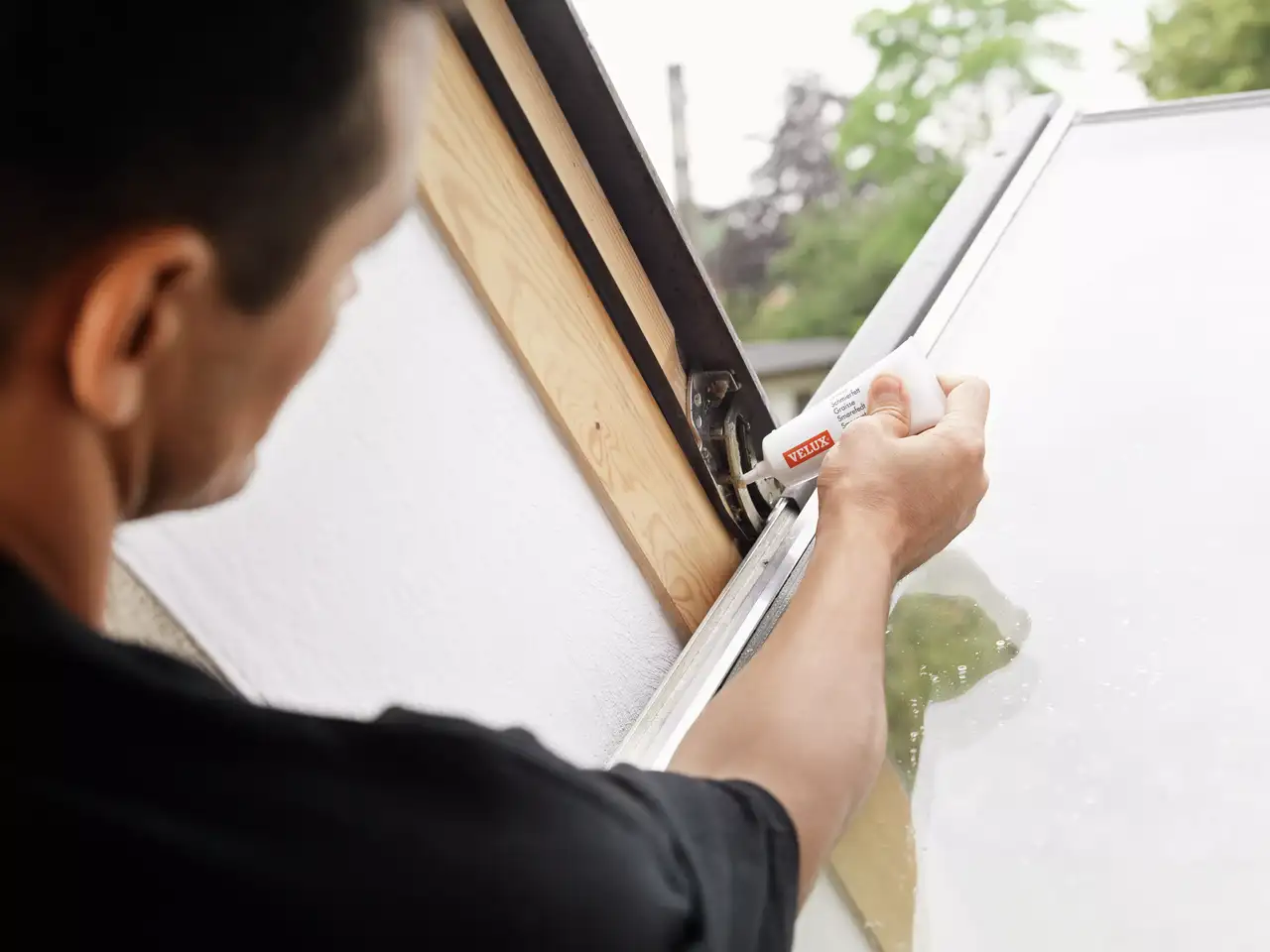 A VELUX szakértő keni a tetőablak zsanérokat.