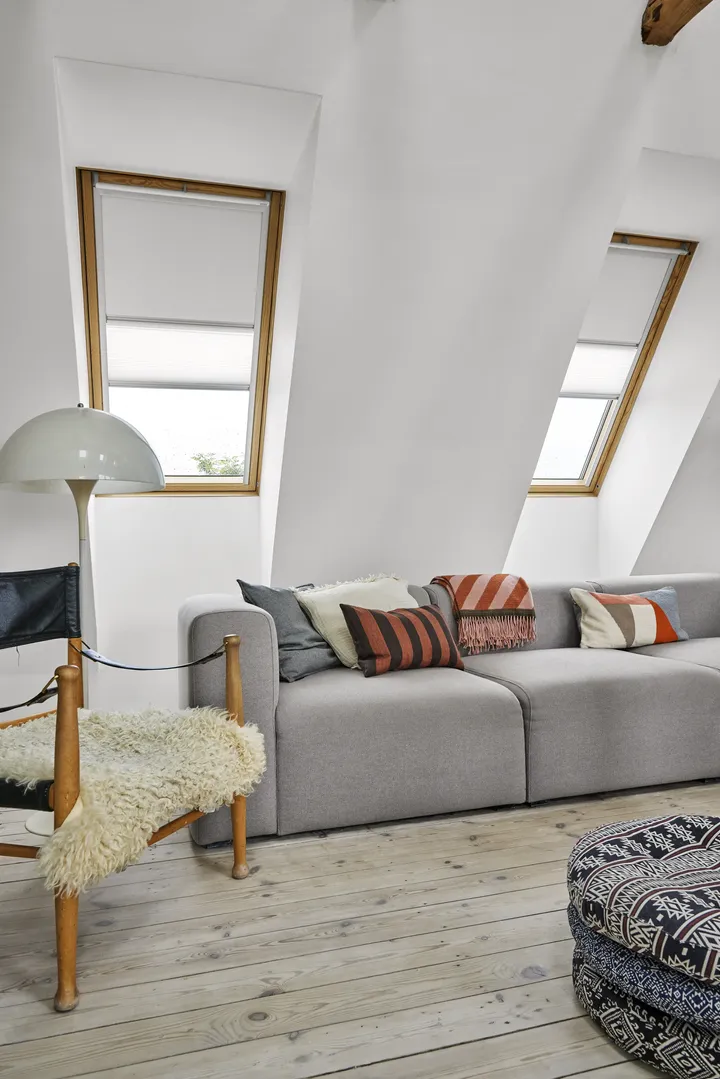 Тавански хол със скосен таван и покривни прозорци VELUX, уютен диван и фотьойл.