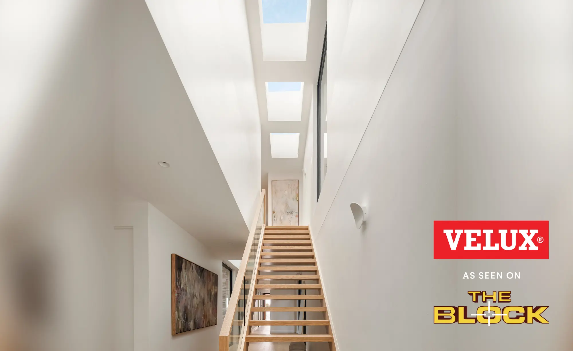 Modern stairwell lit by multiple VELUX flat roof windows above wooden steps.