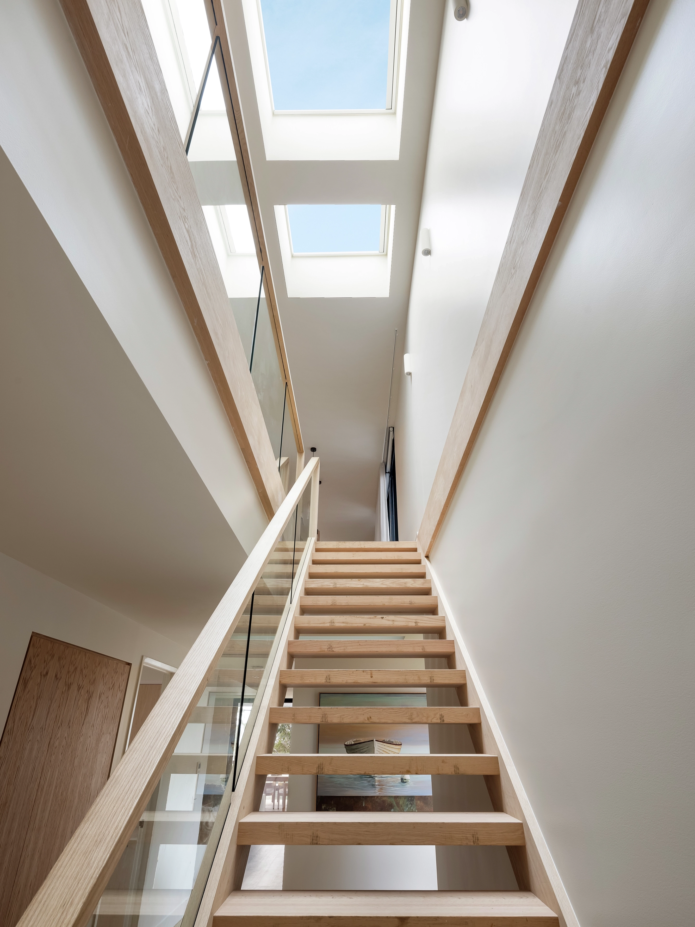 Tall stairwell with wooden stairs lit by three VELUX flat roof windows above.