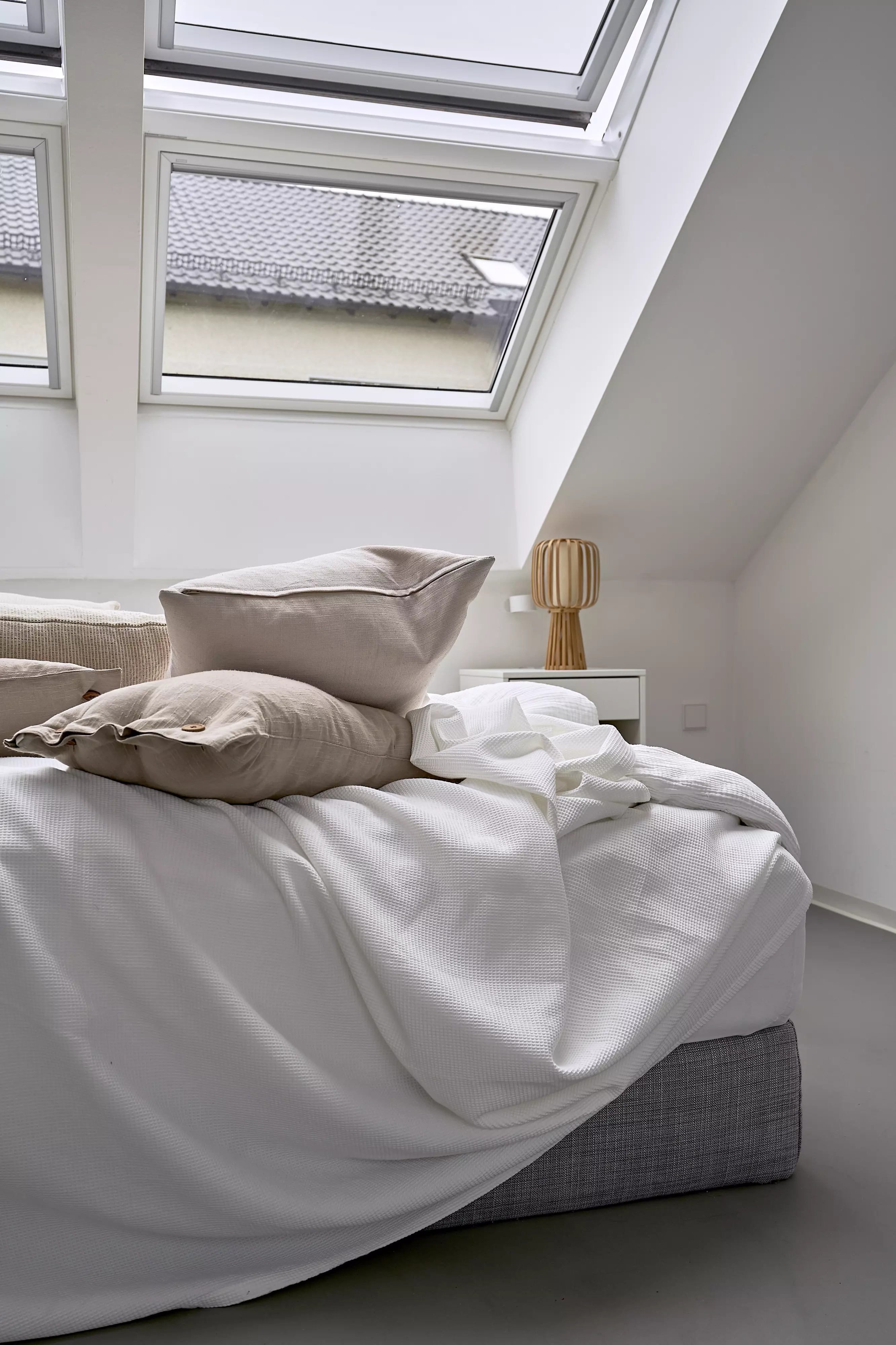 Gemütliches Schlafzimmer mit Bett und Kissen unter natürlichem Licht von VELUX Dachflächenfenstern.