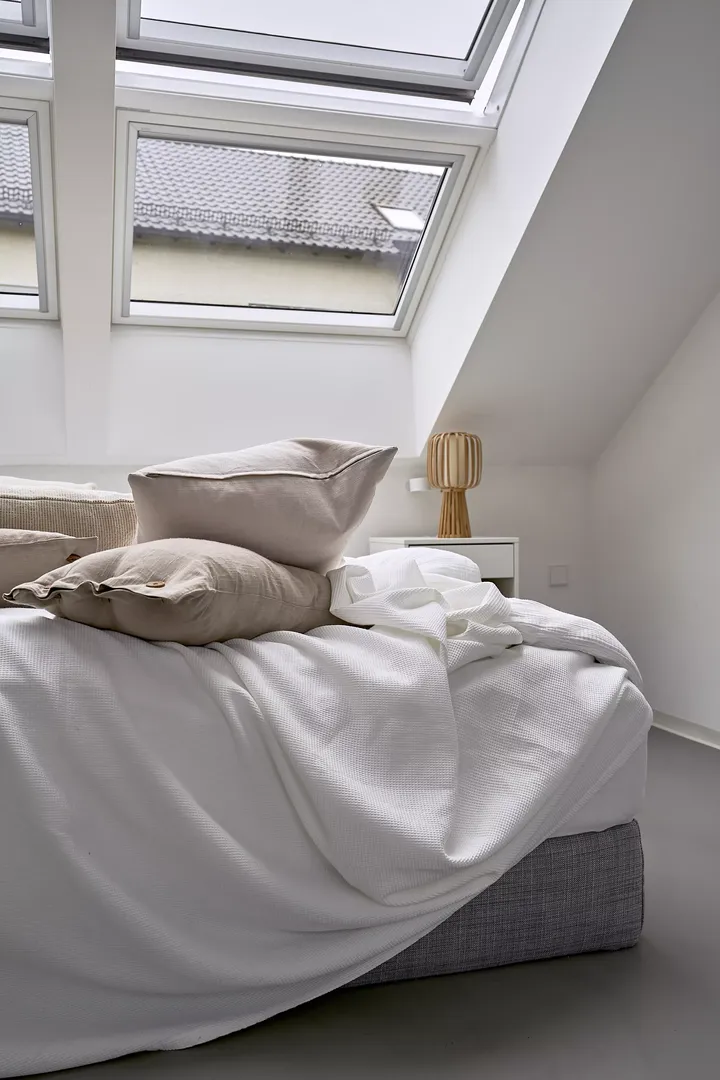 Gemütliches Schlafzimmer mit Bett, Kissen und natürlichem Licht von VELUX Dachflächenfenstern.