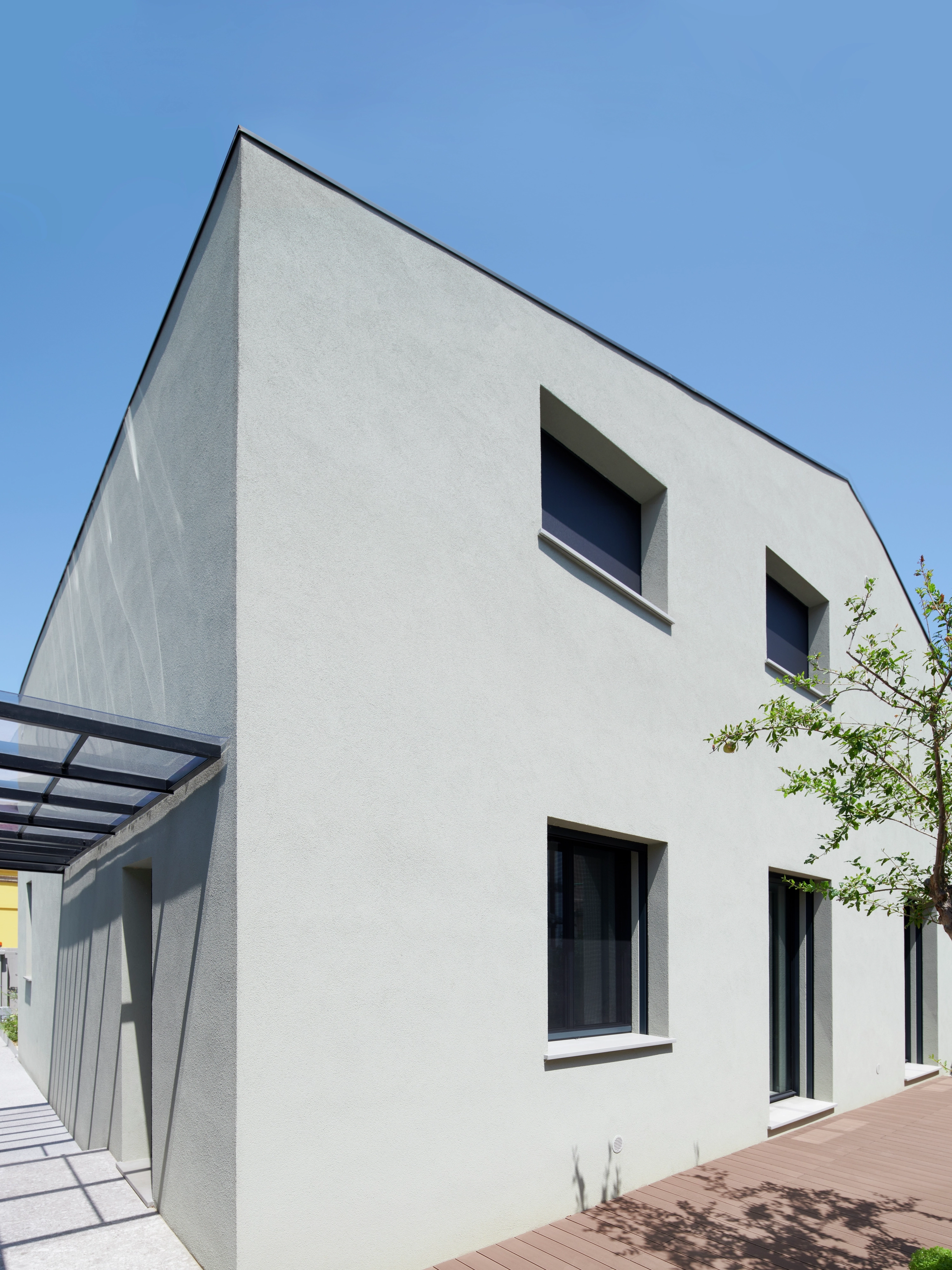Facciata esterna di una villa contemporanea dal design lineare, intonaco chiaro, finestre rettangolari e tettoia d'ingresso in vetro.