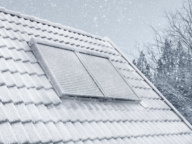 Snow-covered roof with tiles and VELUX roof windows and solar roller shutter.