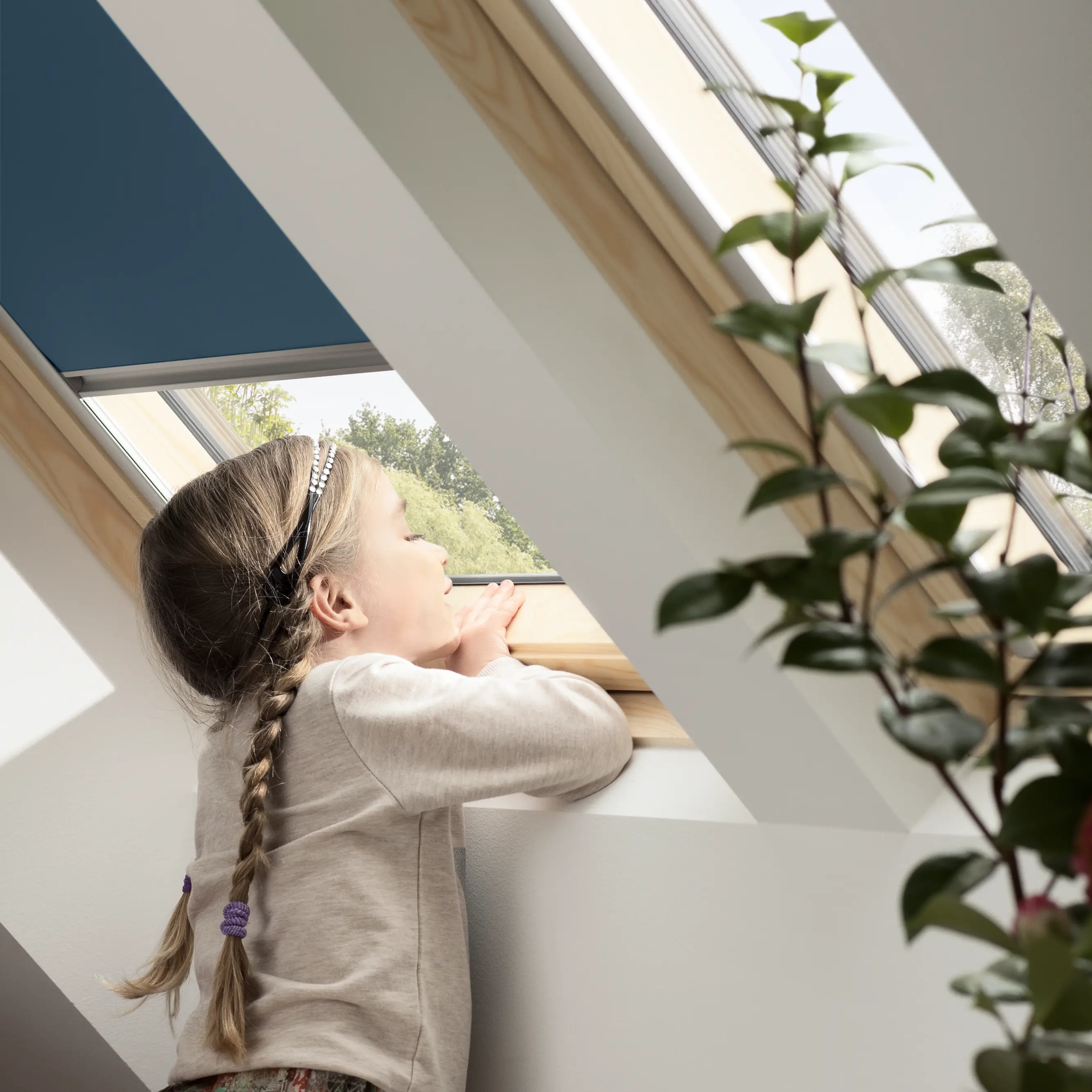 Girl looking through a VELUX roof window in a bright attic room.