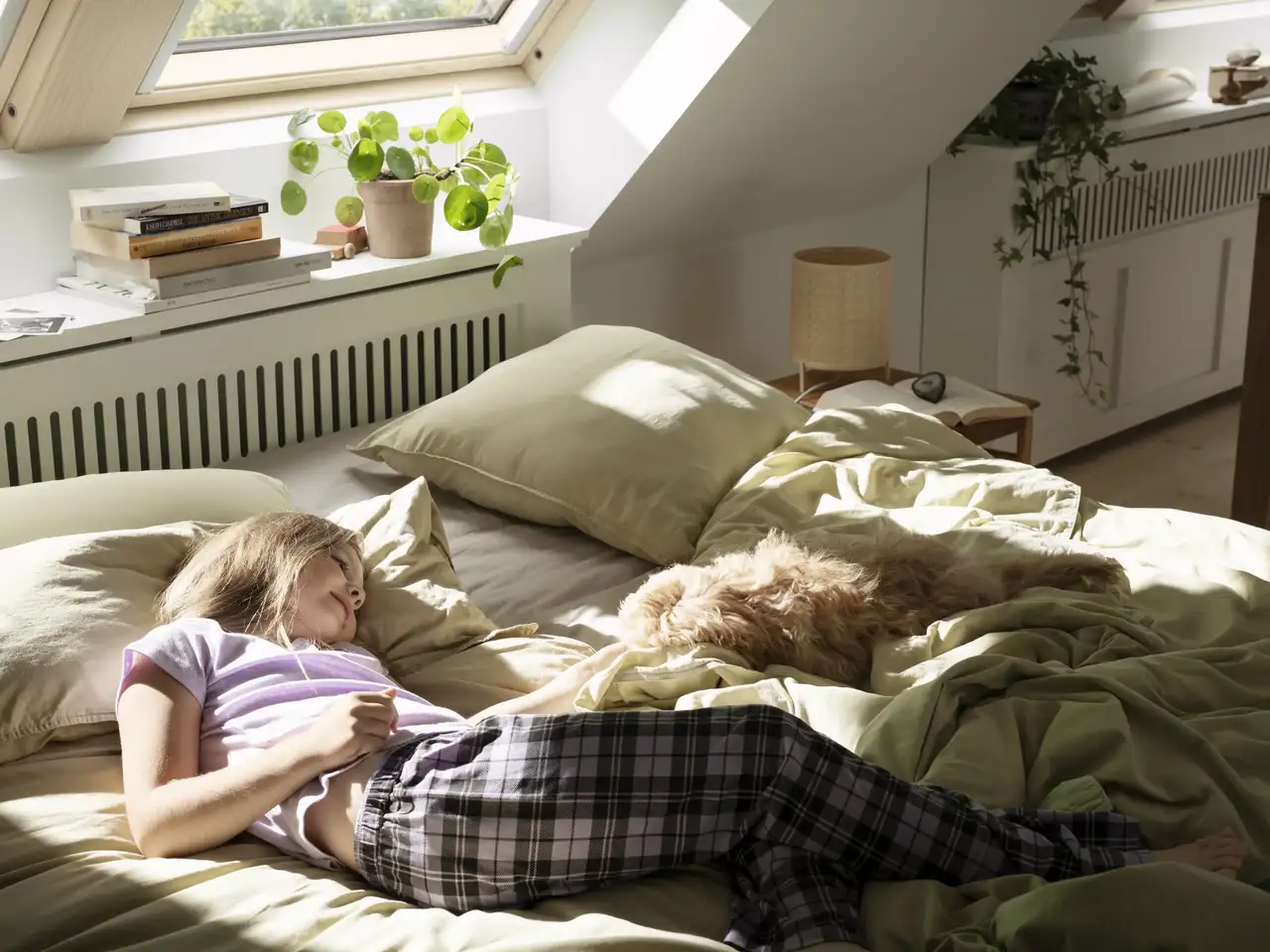 Une fillette caresse son chien sur le lit sous la lucarne | Magazine VELUX