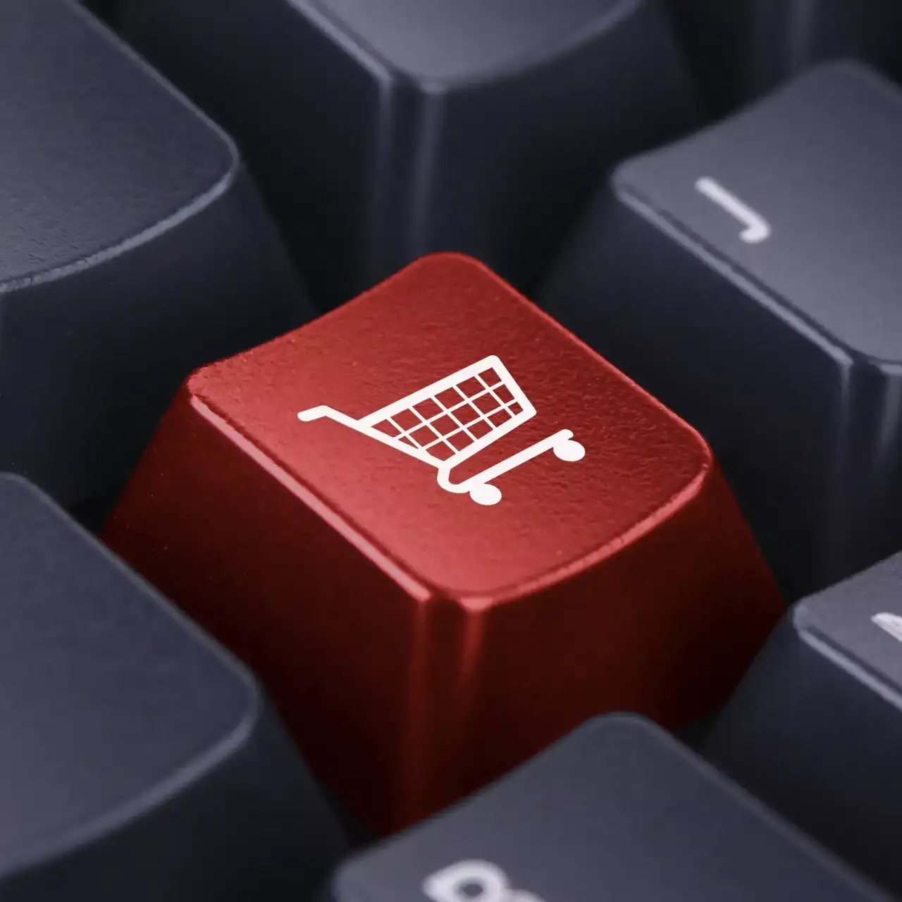 Nahaufnahme eines roten Schlüssels mit einem Einkaufswagen-Symbol auf einer Tastatur, die das Online-Shopping darstellt.