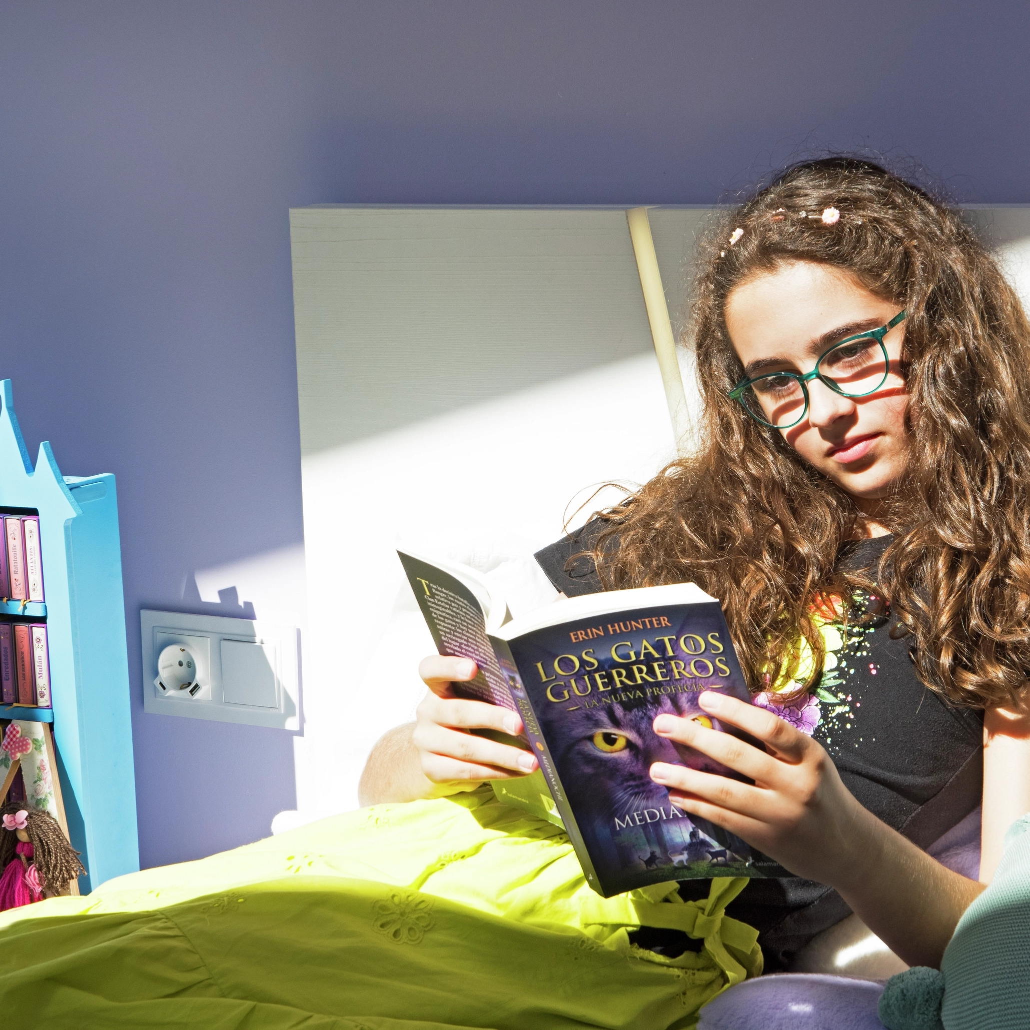 Chica joven leyendo un libro en su cama iluminada por luz natural