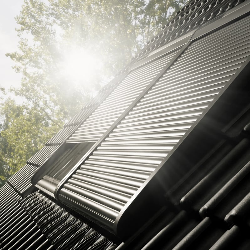 Sunlit roof with metal panels and VELUX window, surrounded by trees.