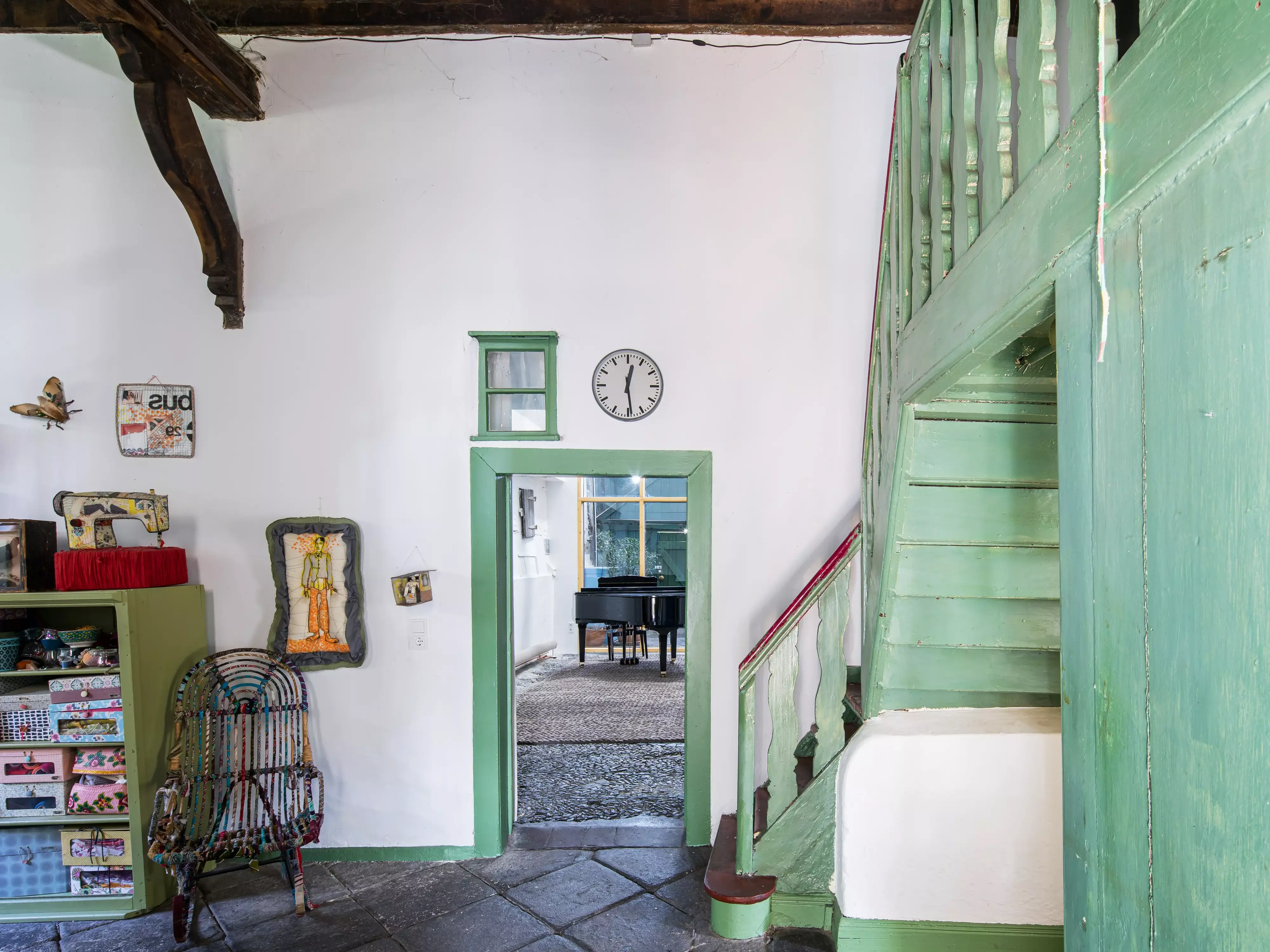 Escalier vintage vert en bois dans une maison rustique avec un décor éclectique et un grand piano visible.