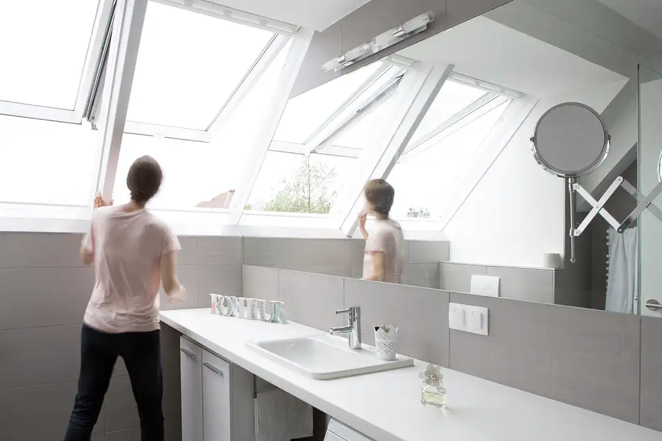 Personne debout devant des fenêtres de toit ouvertes dans la salle de bain.