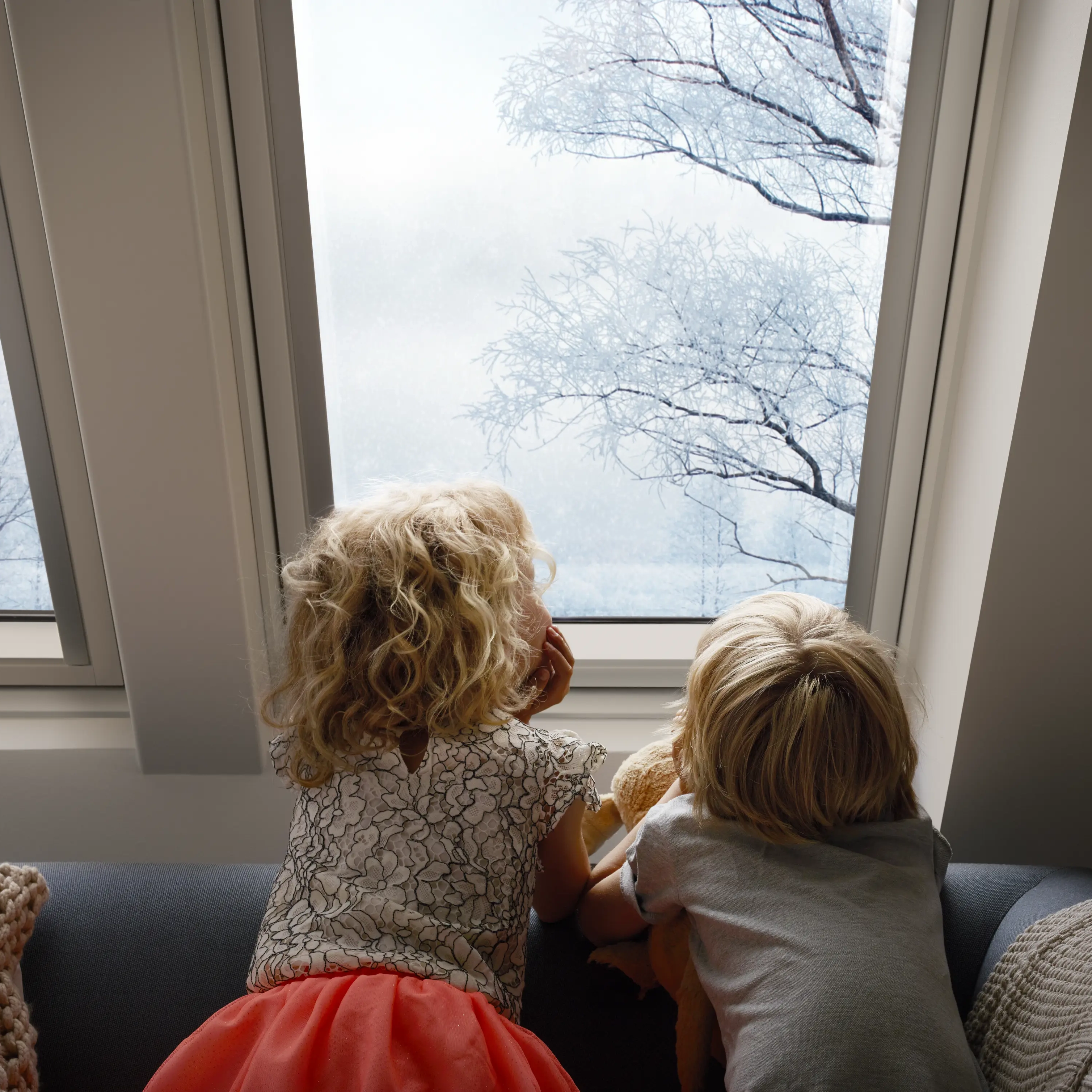 Enfants assis sur un canapé, regardant les arbres enneigés par une fenêtre de toit VELUX.
