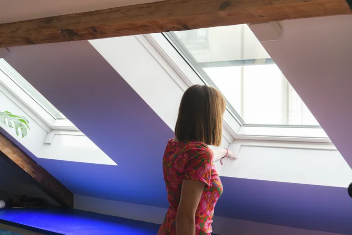 Жена регулира покривен прозорец VELUX в таванско помещение със скосена таванна конструкция.