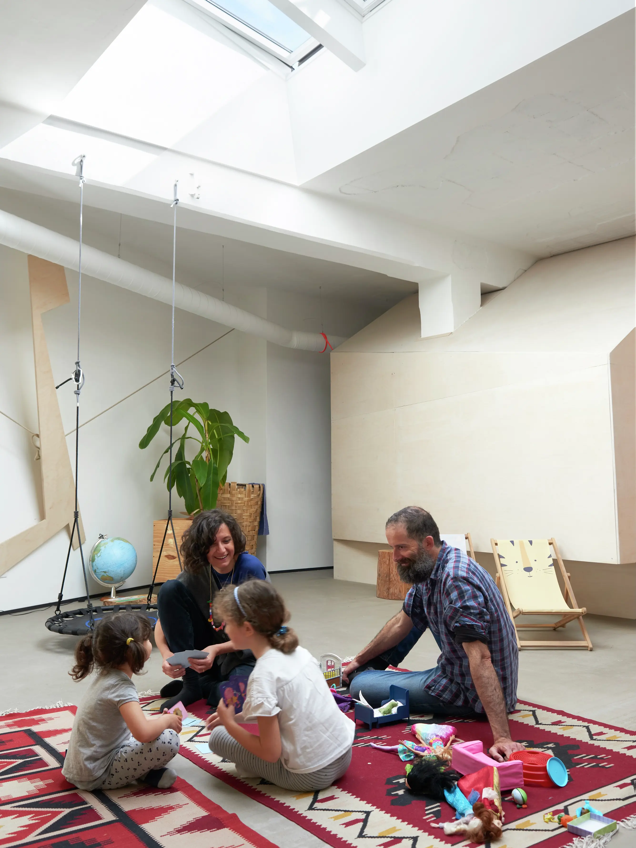 Famiglia che gioca in un soggiorno illuminato da una finestra per tetti VELUX, con giocattoli e un'altalena.