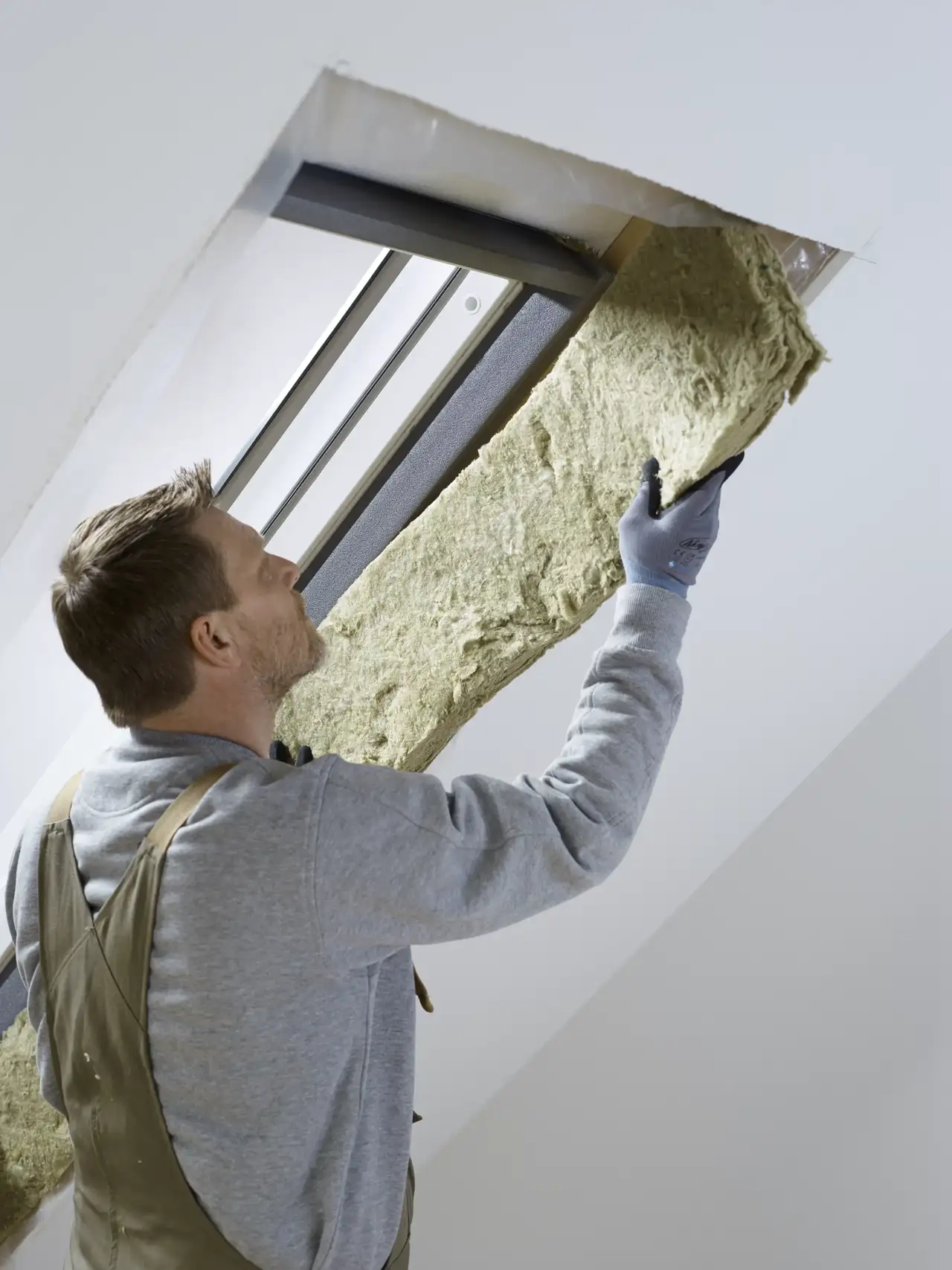 Hombre instalando aislamiento en una ventana de tejado en un ático 