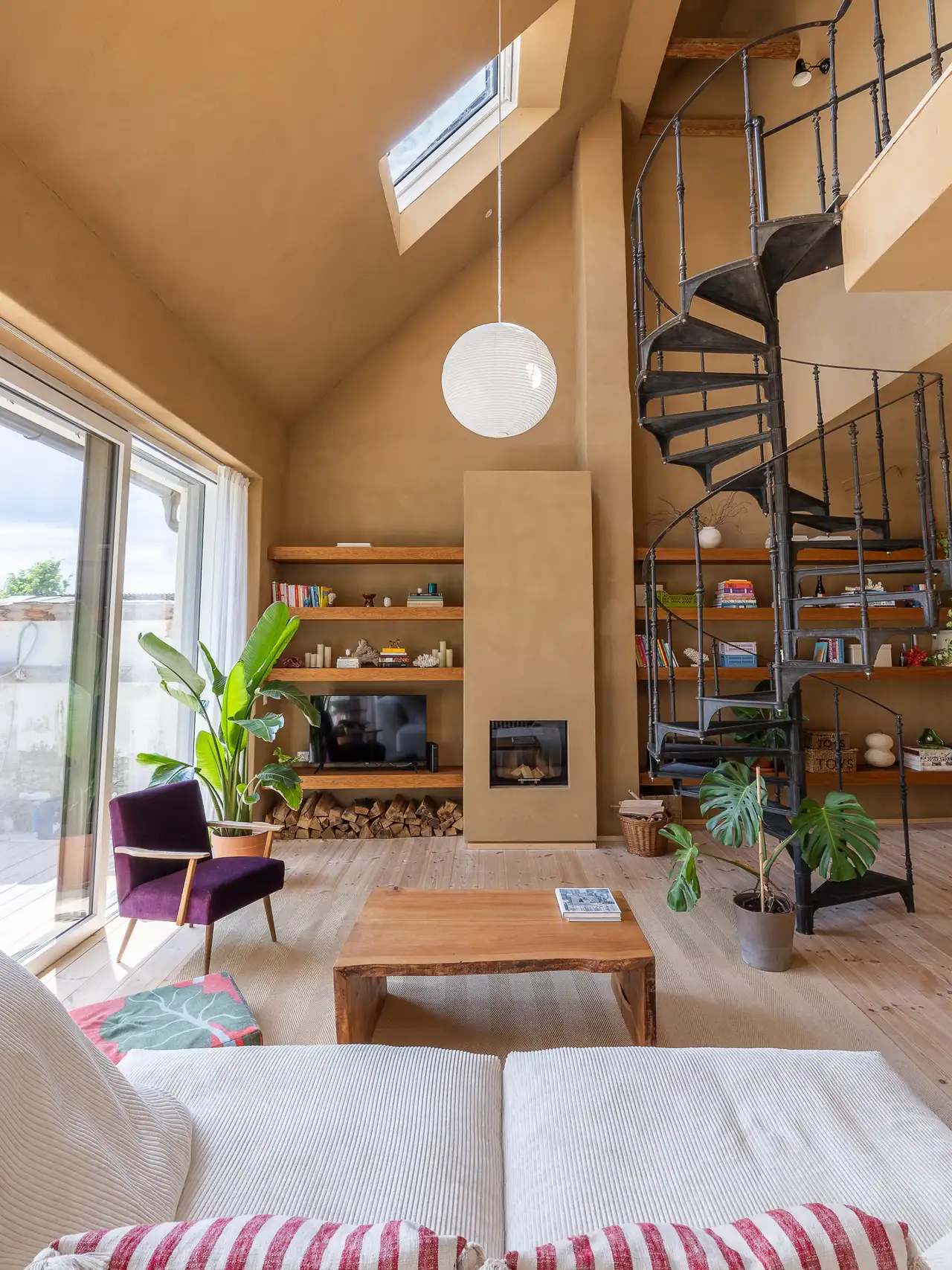 Living room with sloped ceiling, VELUX roof window, and spiral staircase.