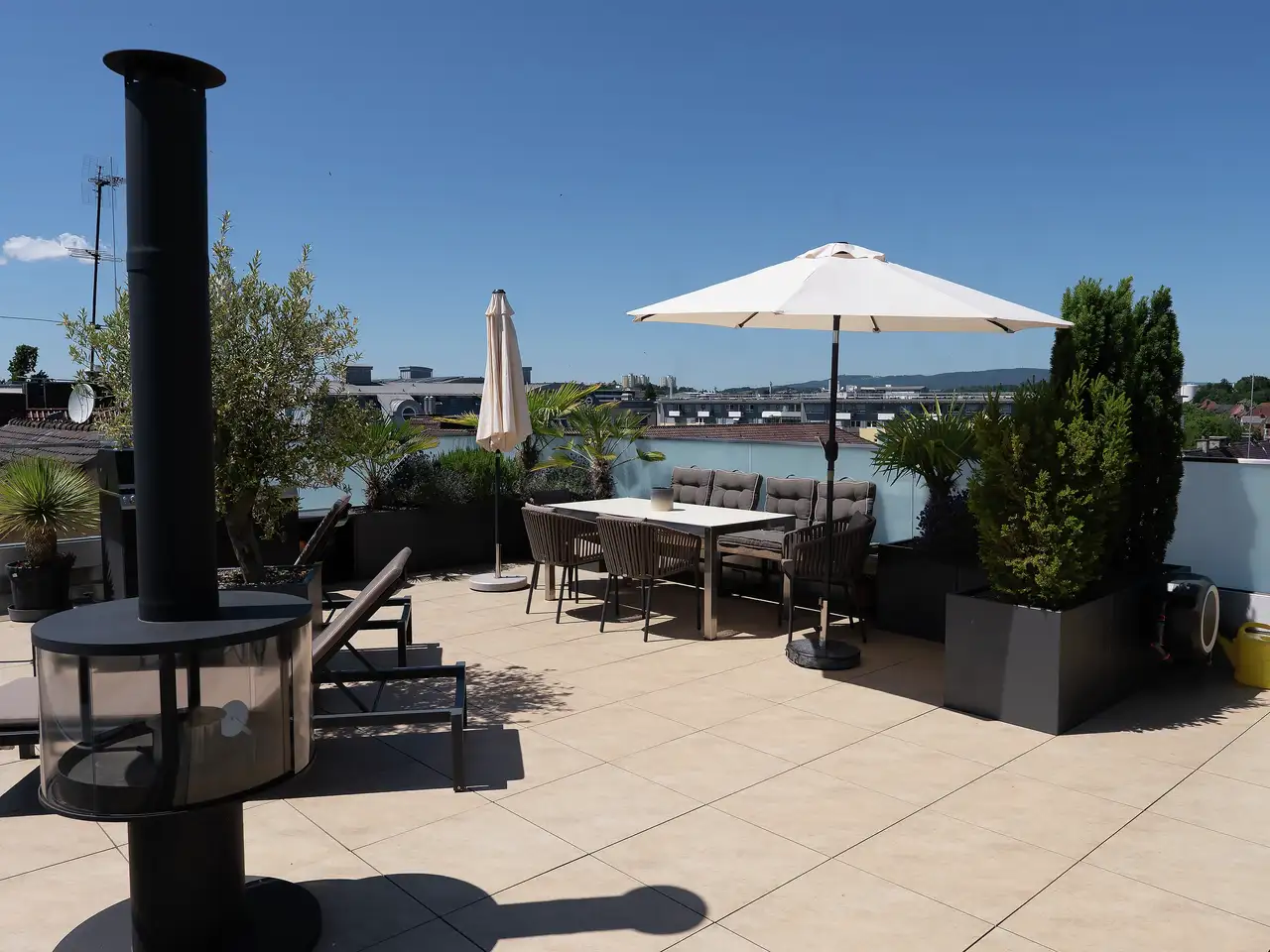 terrasse sur toit plat avec coin repas, parasol et vue sur les toits de la ville 