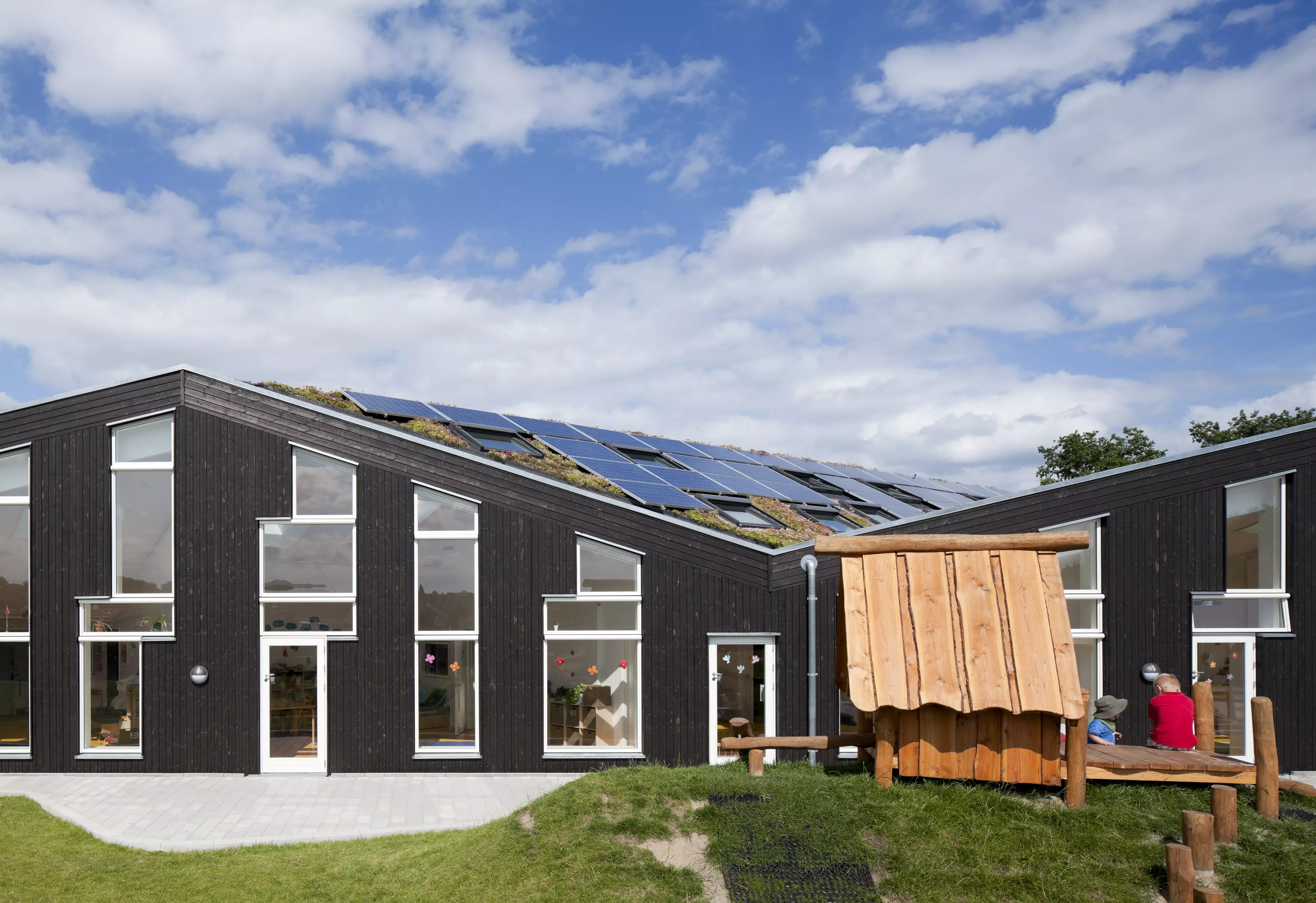 Daycare facility with solar panels on sloped roof and wooden play area.
