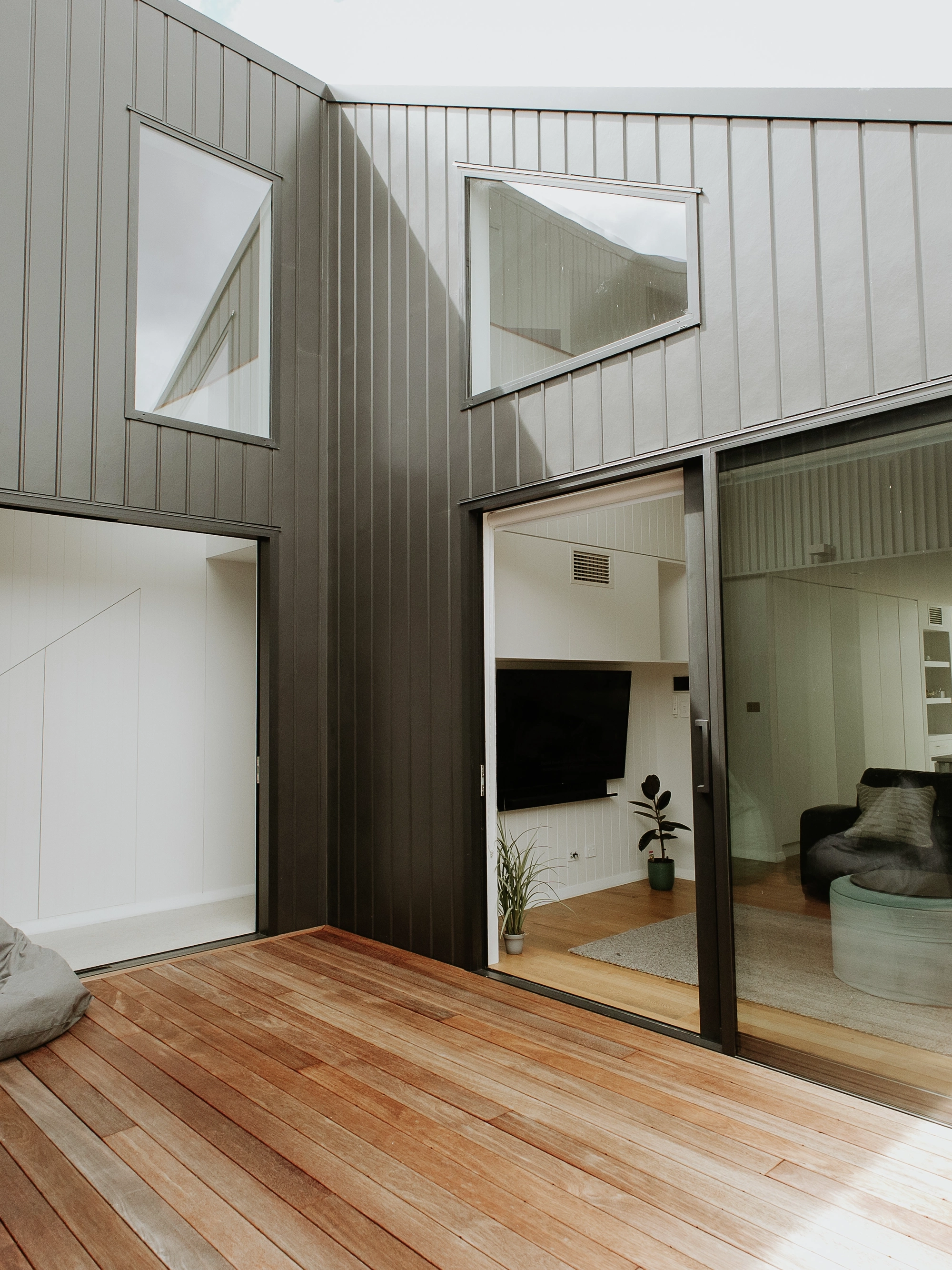 Modern metal-clad courtyard with timber deck and large sliding glass doors to living room.