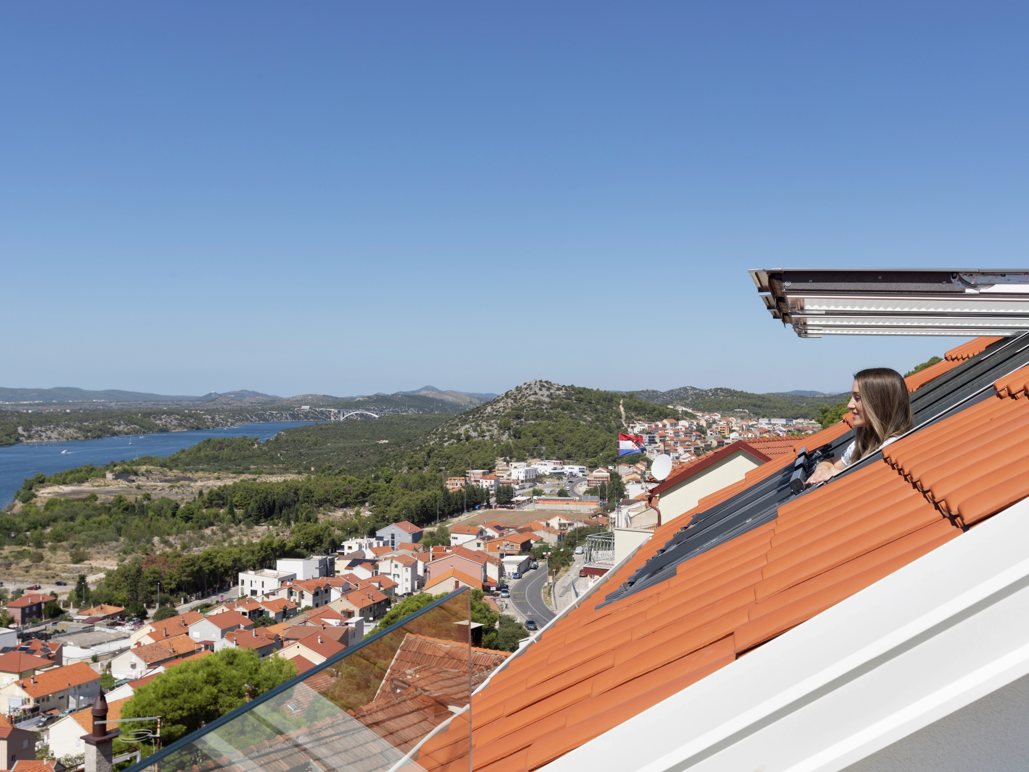 Open VELUX roof window with scenic view of hills and river.
