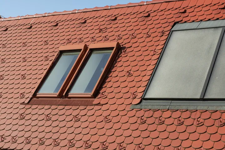Nahaufnahme eines roten Ziegeldachs mit einem traditionellen und einem VELUX Dachflächenfenster.