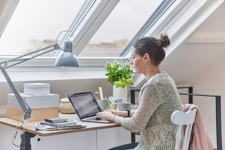 Frau sitzt am Schreibtisch unter Dachfenstern | VELUX Magazin