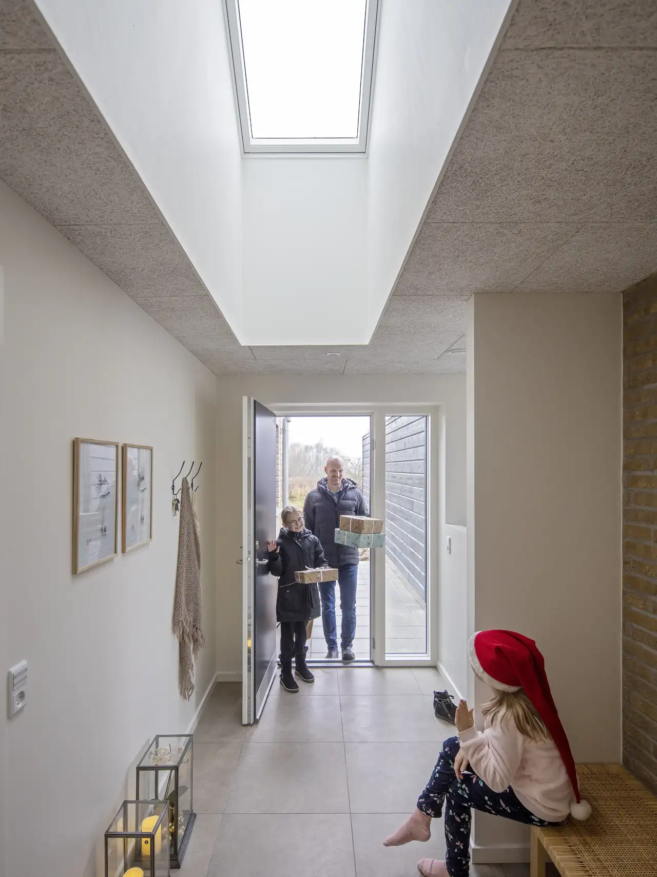 Ingresso decorato per Natale con lanterne e finestra per tetti VELUX, una bambina accoglie la famiglia con pacchi regalo.