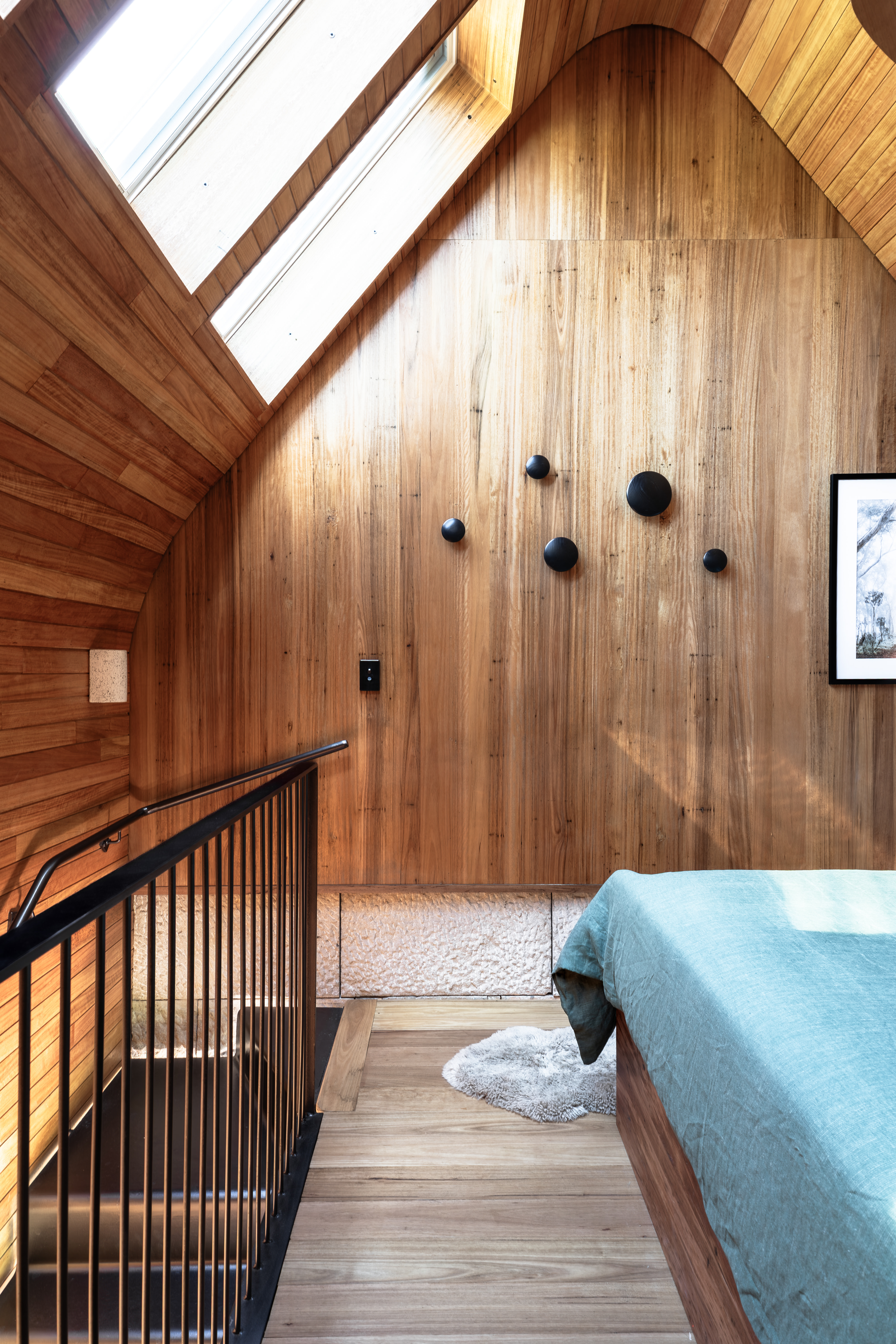 Wood-clad attic bedroom with VELUX roof window above bed and staircase railing.