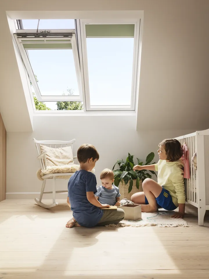 Kinder sitzen spielend auf dem Boden unter dem gekippten, elektrischen Dachfenster | VELUX Magazin