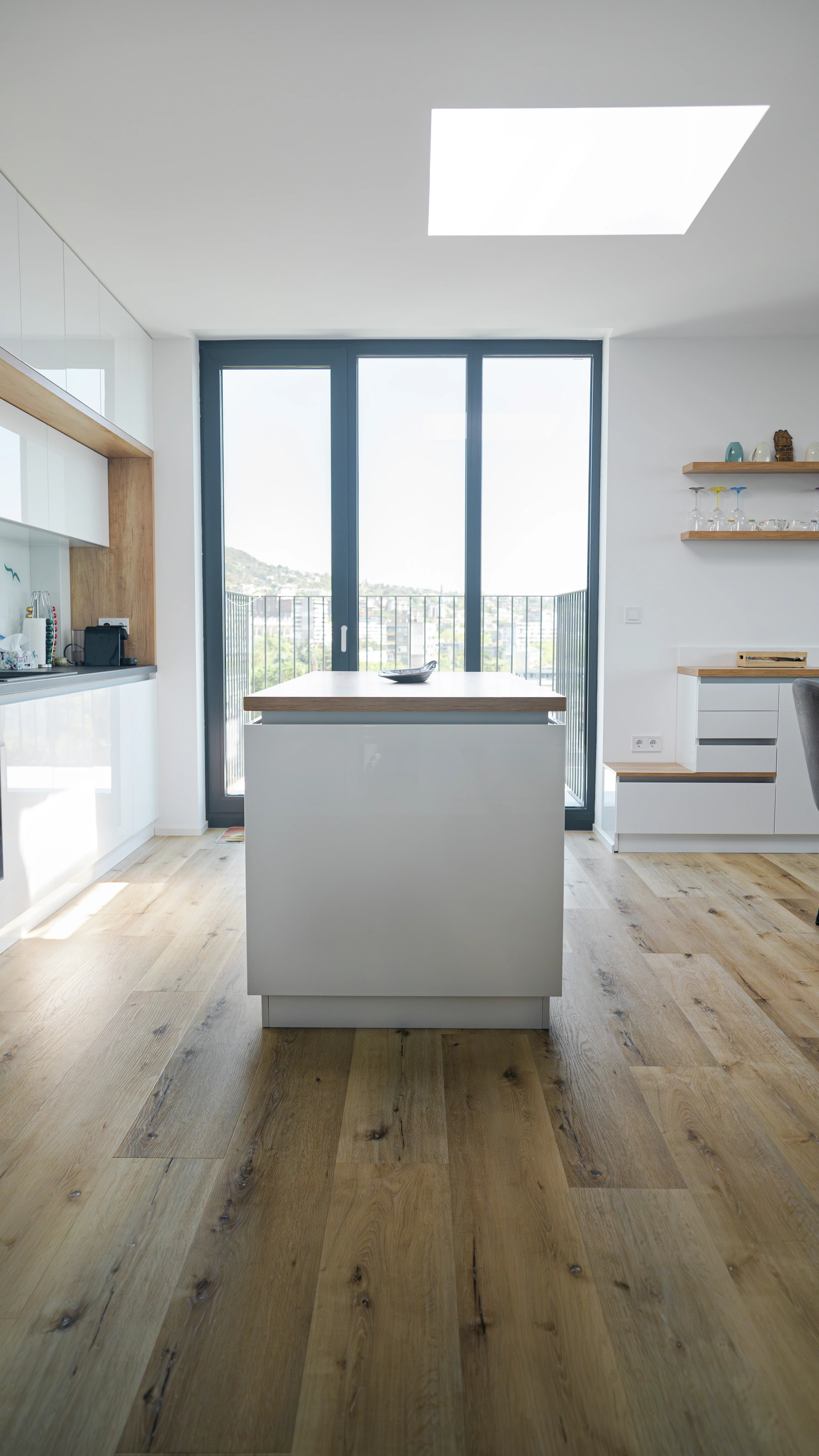 Modern kitchen with island, VELUX flat roof window and balcony doors to a city view.
