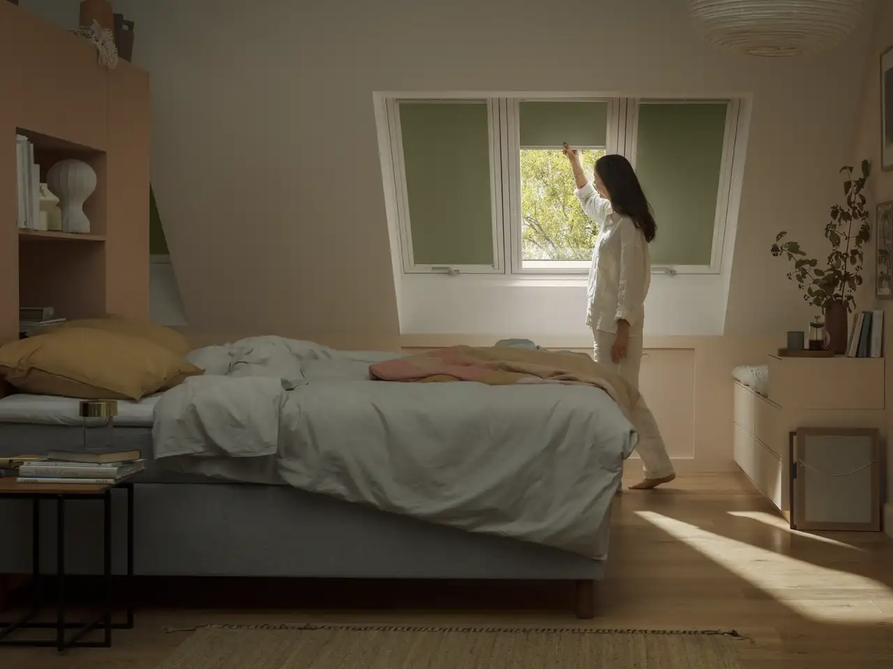Attic bedroom with sloped ceiling and VELUX roof window, woman adjusting blinds.
