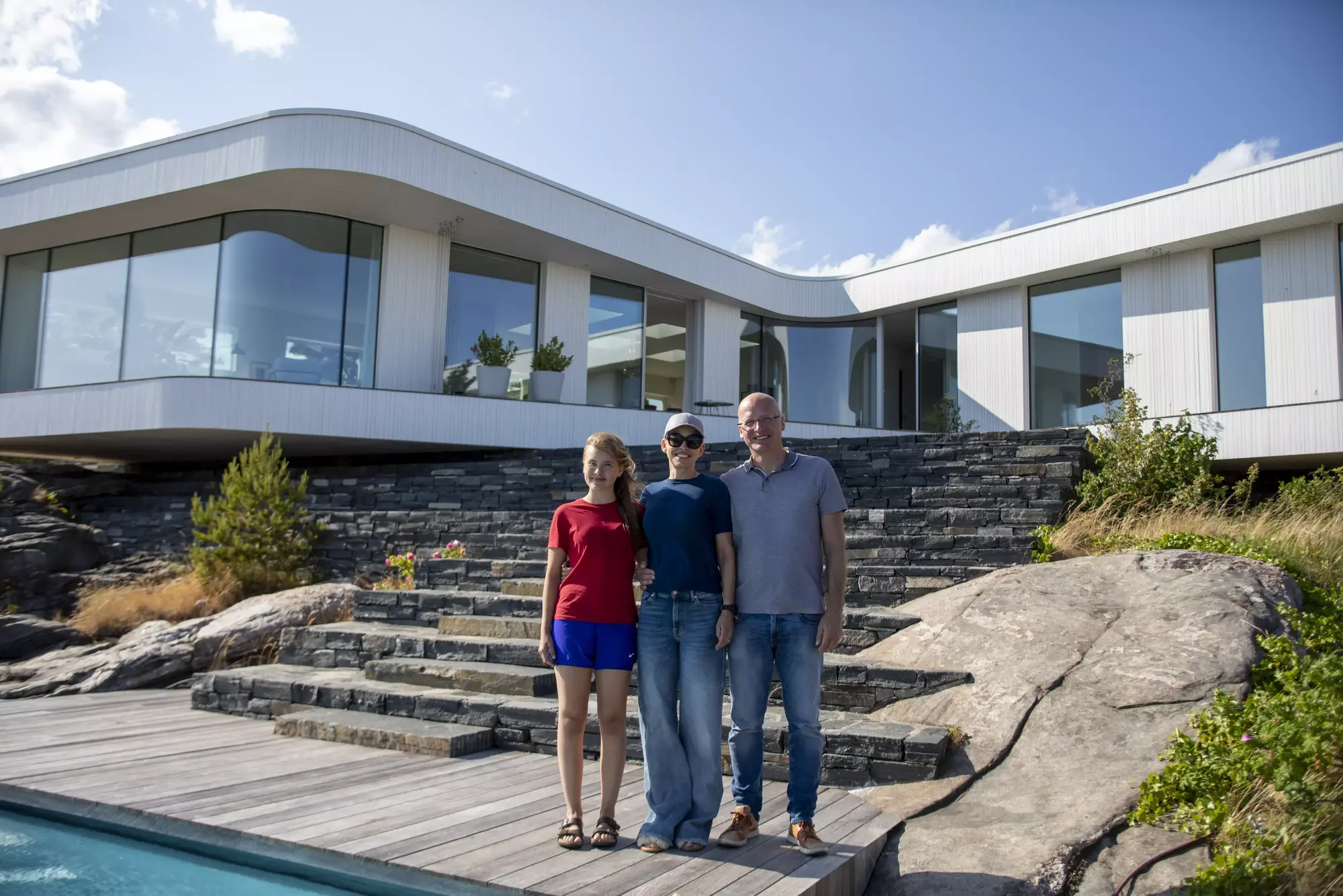 Family standing next to a pool and in front of their home