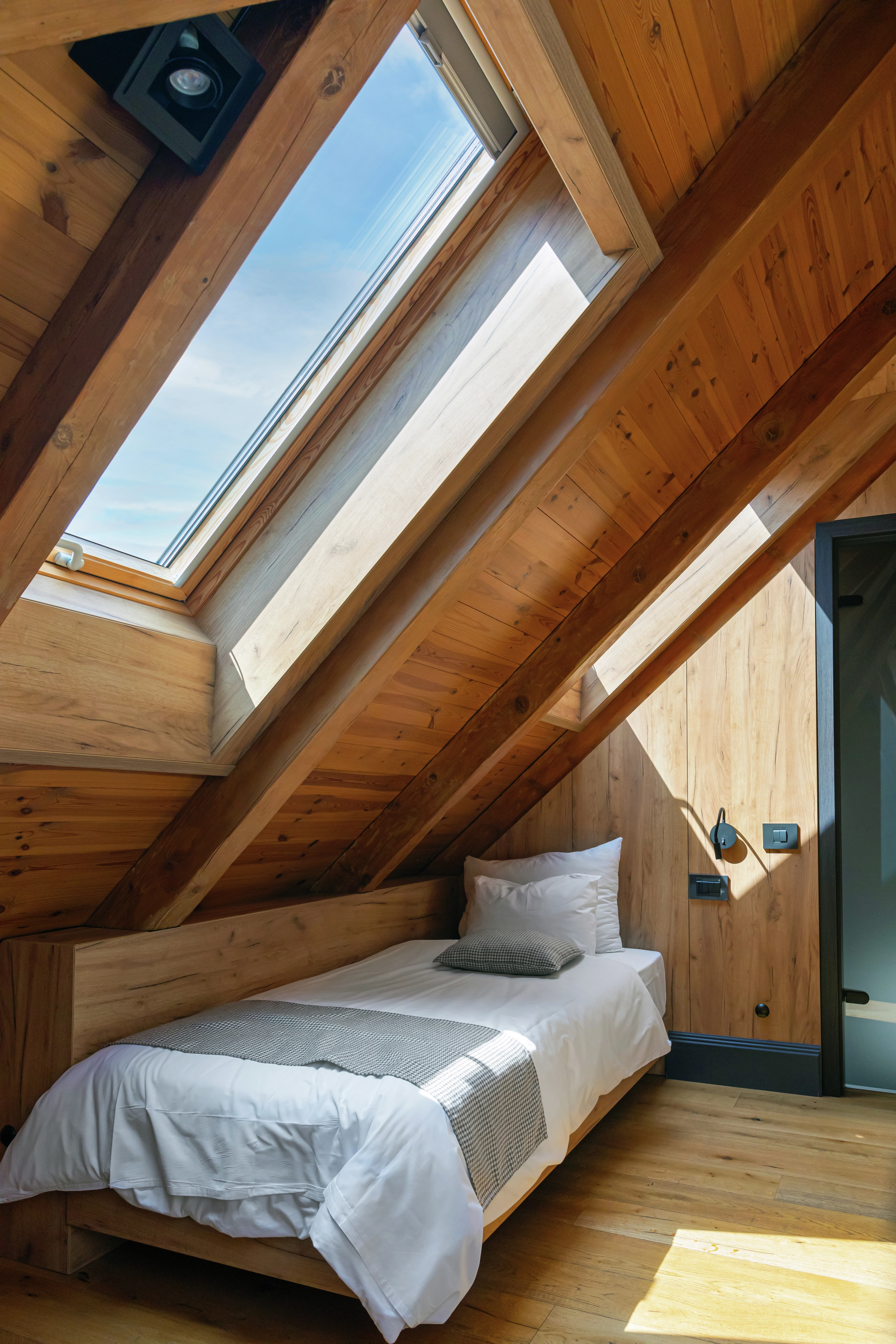 Pokój hotelowy na poddaszu ze skośnym, drewnianym sufitem i oknem dachowym VELUX