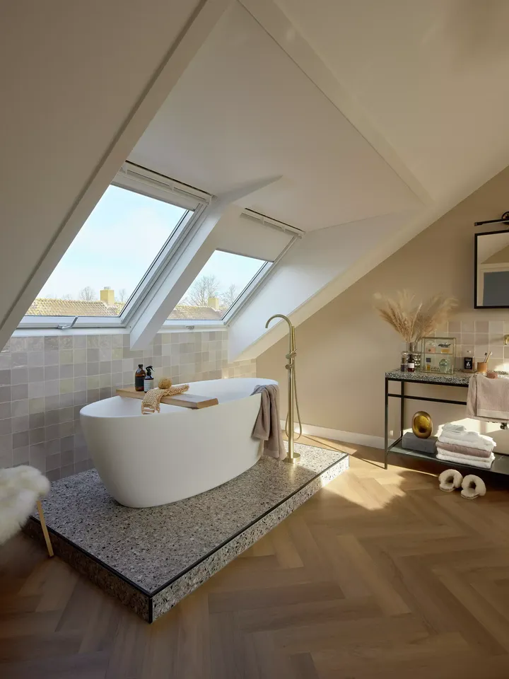 Modernes Badezimmer im Dachboden mit freistehender Badewanne und VELUX Dachflächenfenstern, die für reichlich Sonnenlicht sorgen.