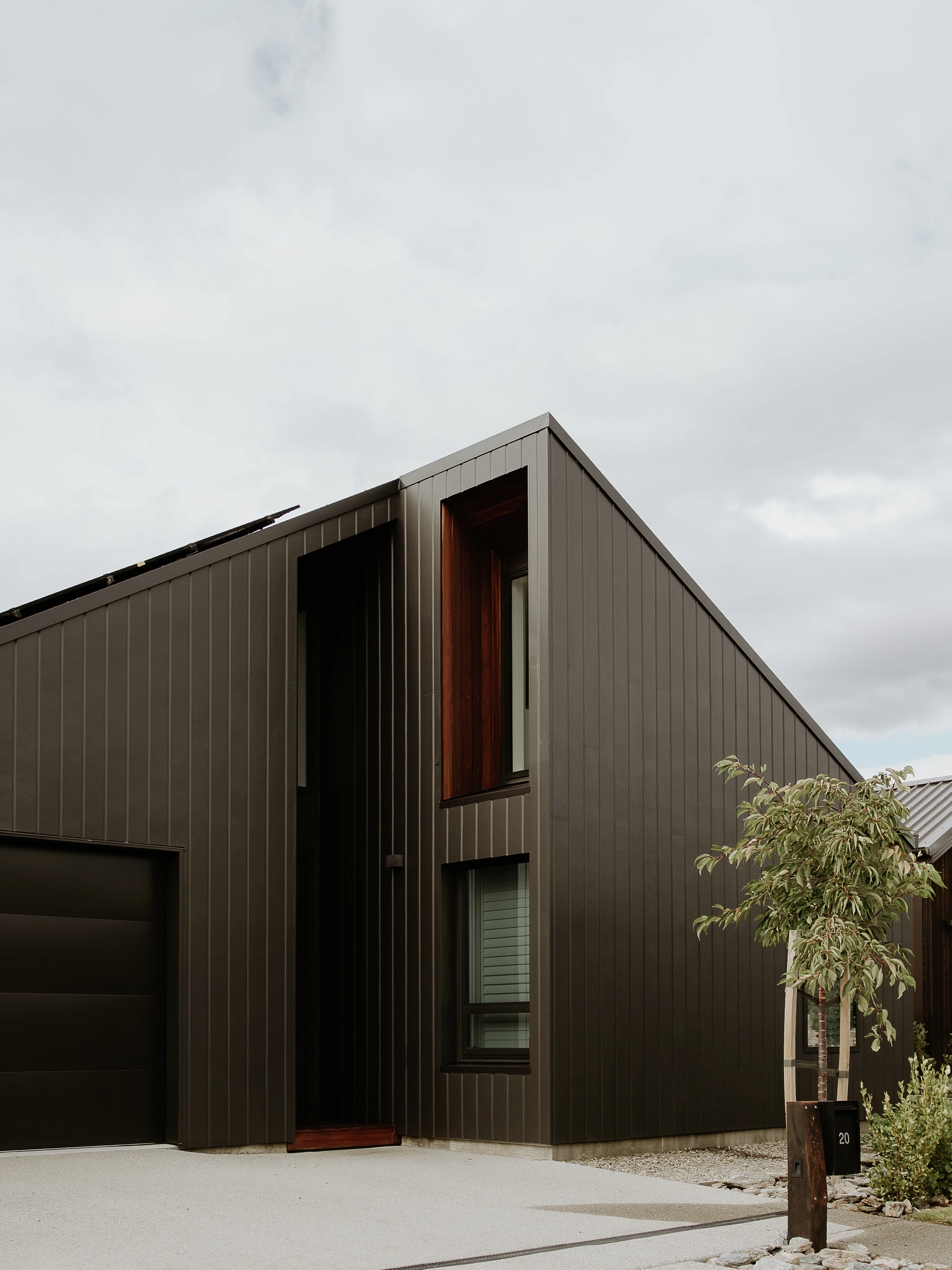 Contemporary dark metal-clad single-family house with low-pitch roof and garage on a cloudy day.