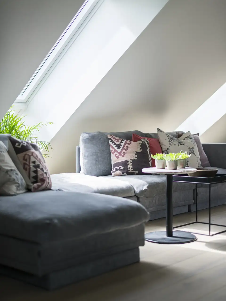 Canapé gris agrémenté de coussins aux textures douces, sous des fenêtres de toit VELUX diffusant une lumière délicate 