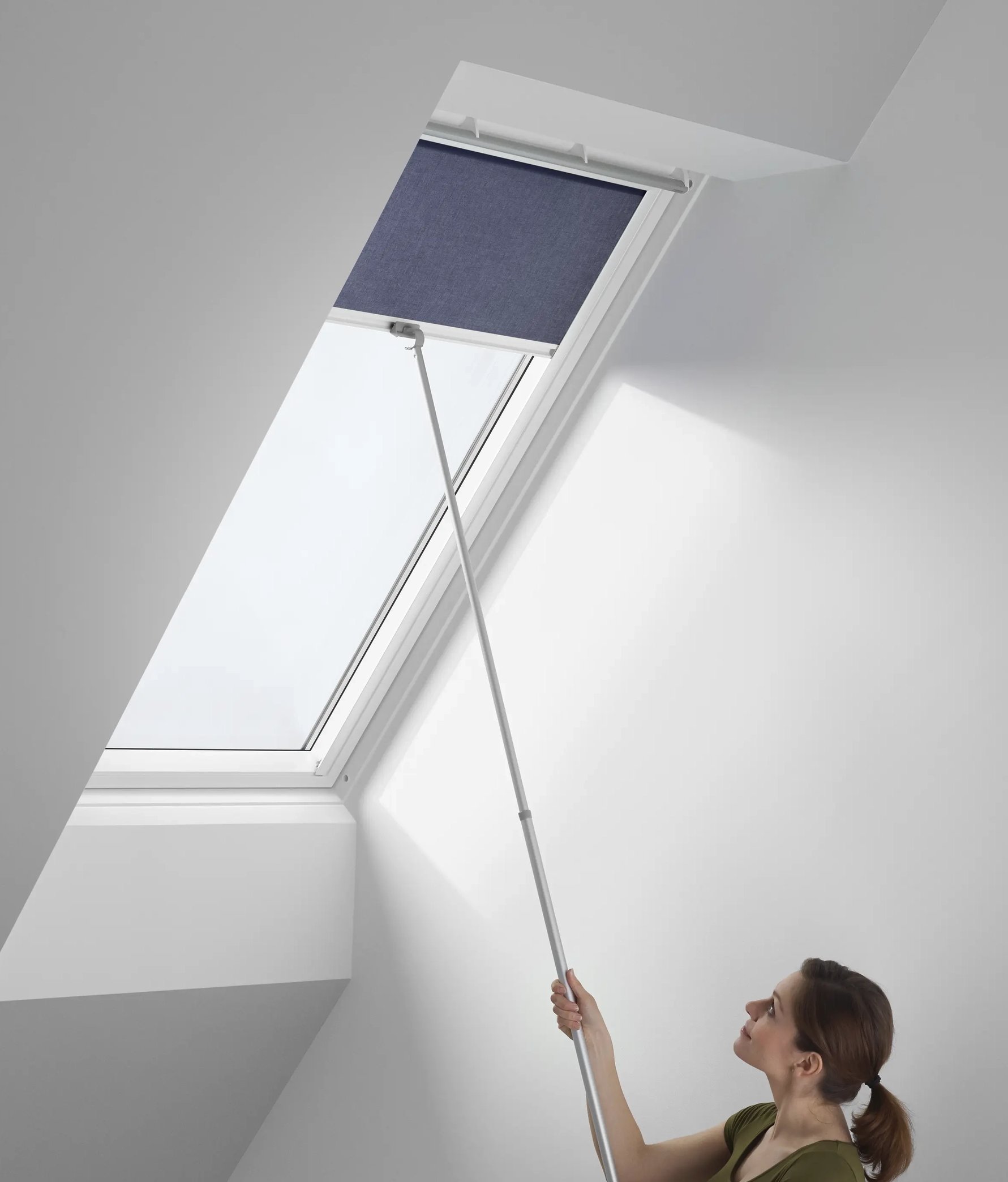 Person adjusting blind on VELUX roof window with a pole.