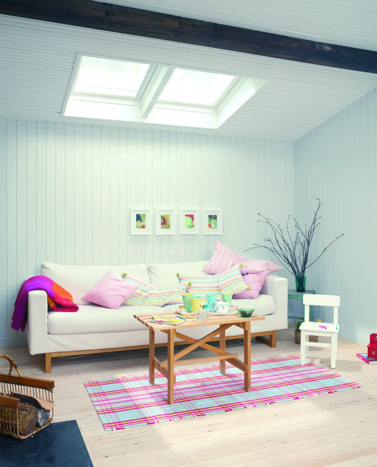Wohnzimmer im Danish-Pastel-Einrichtungsstil mit pastellfarbenen Kissen, heller Couch, Holz-Couchtisch und buntem Teppich unter Dachfenstern | VELUX Magazin